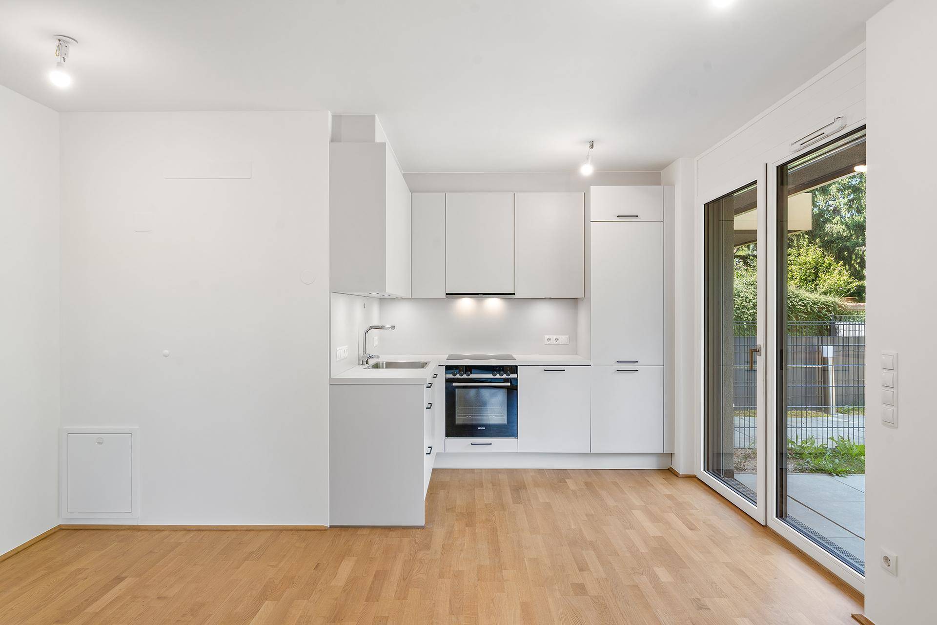 Moderne Einbauküche in Weiß mit Kochfeld und Backofen, offen zum Wohnbereich.