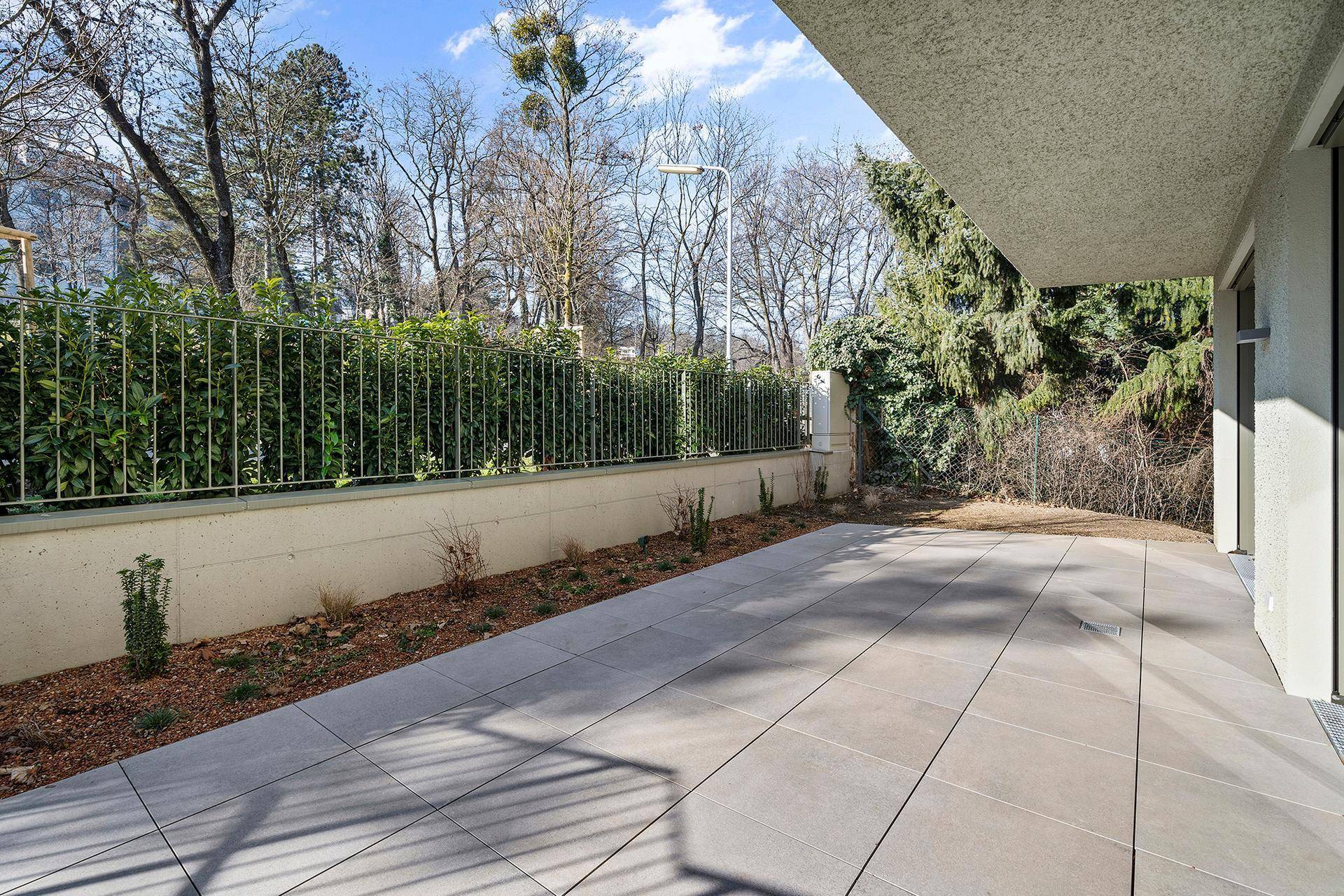 Geräumige gepflasterte Terrasse mit angrenzendem Gartenbereich und grüner Hecke.