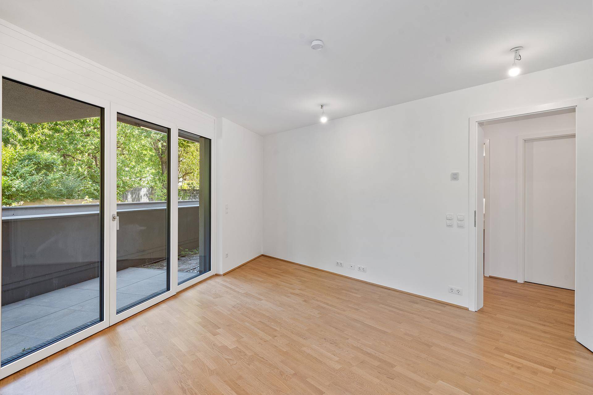 Geräumiges Wohnzimmer mit Holzboden und großen Schiebetüren zum Balkon.