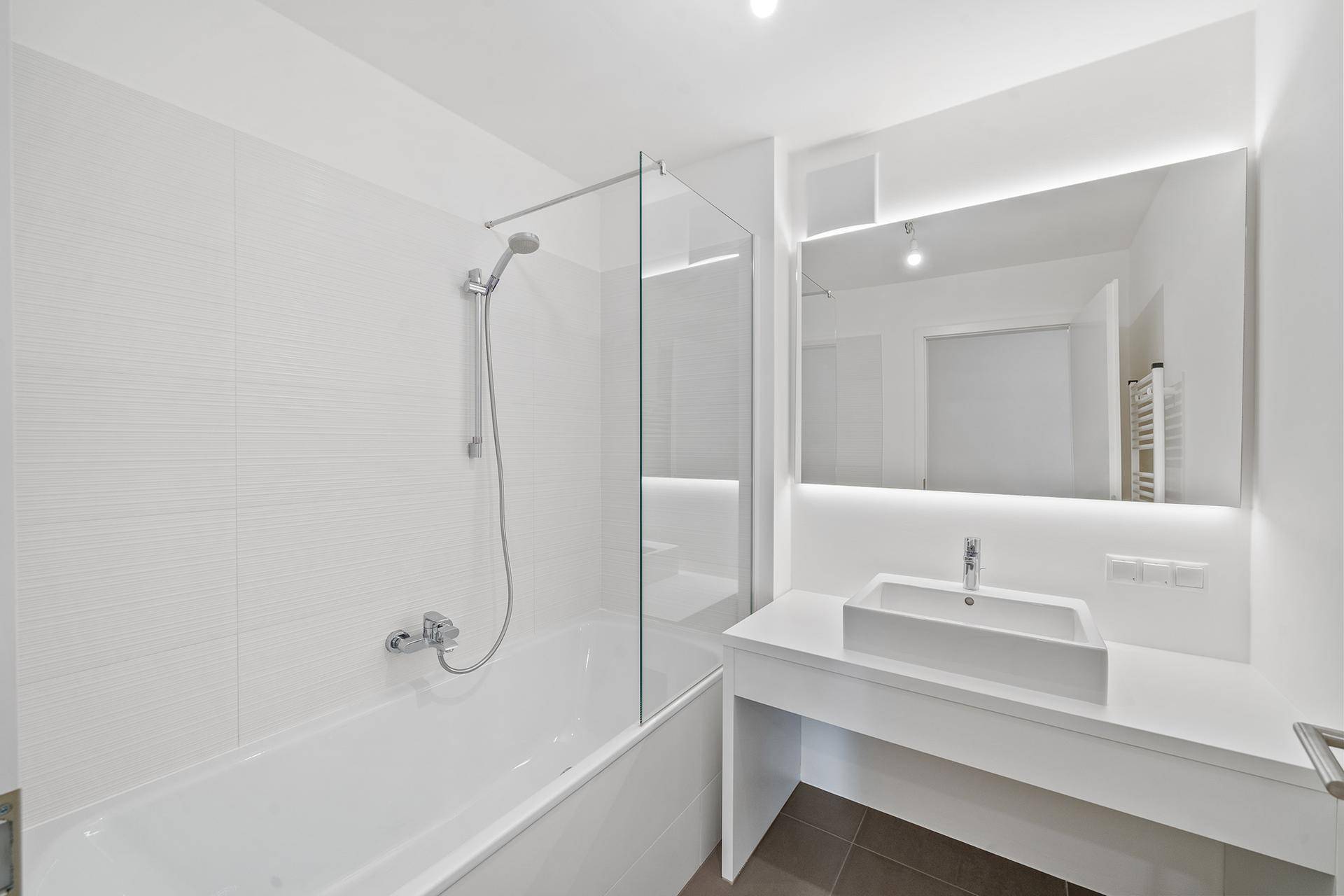 Modernes Badezimmer mit Badewanne, Duschabtrennung aus Glas und beleuchtetem Spiegel.