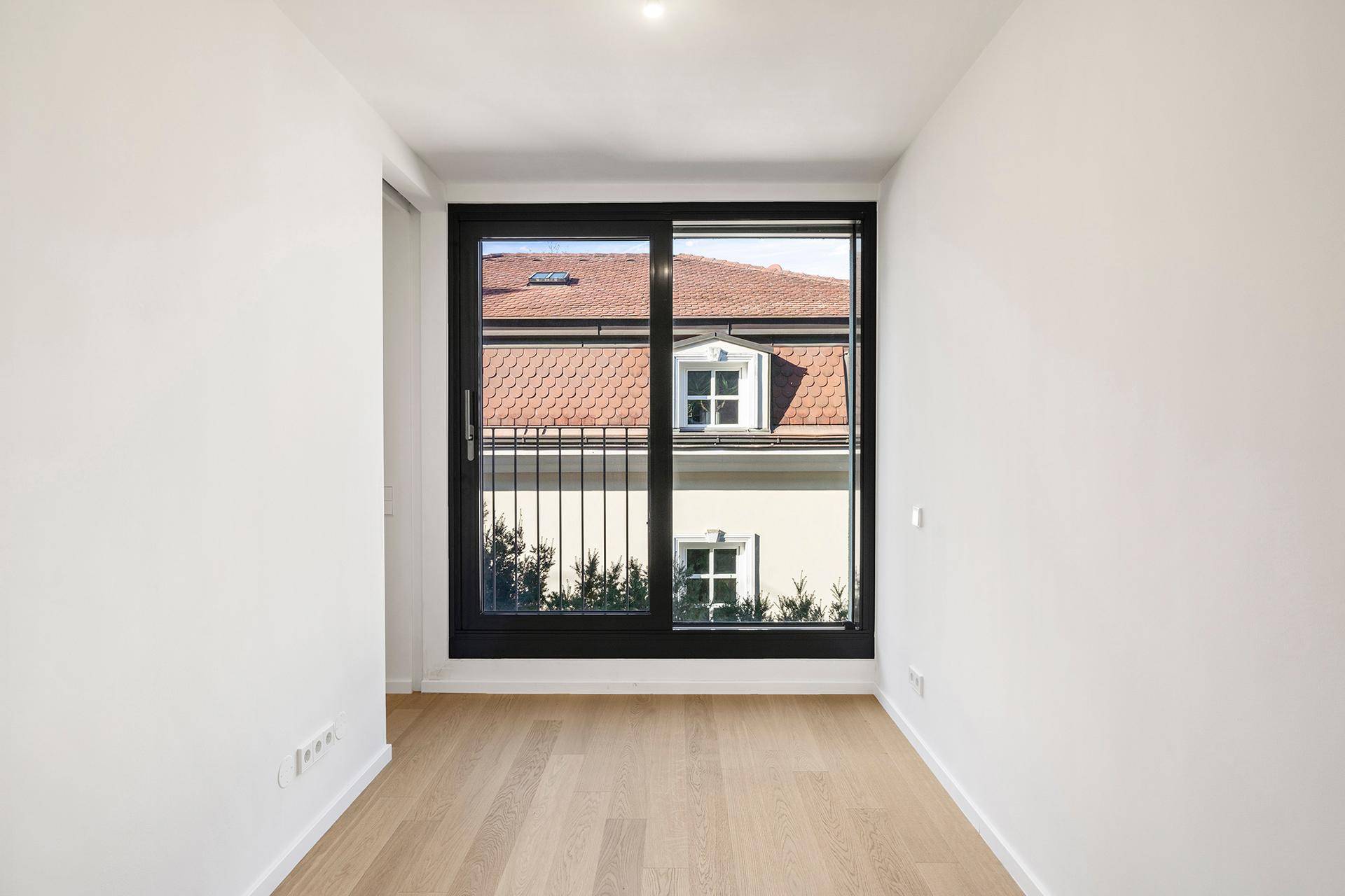 Ruhiges Zimmer mit großem Fenster und Blick auf die umliegenden Dächer und Bäume.