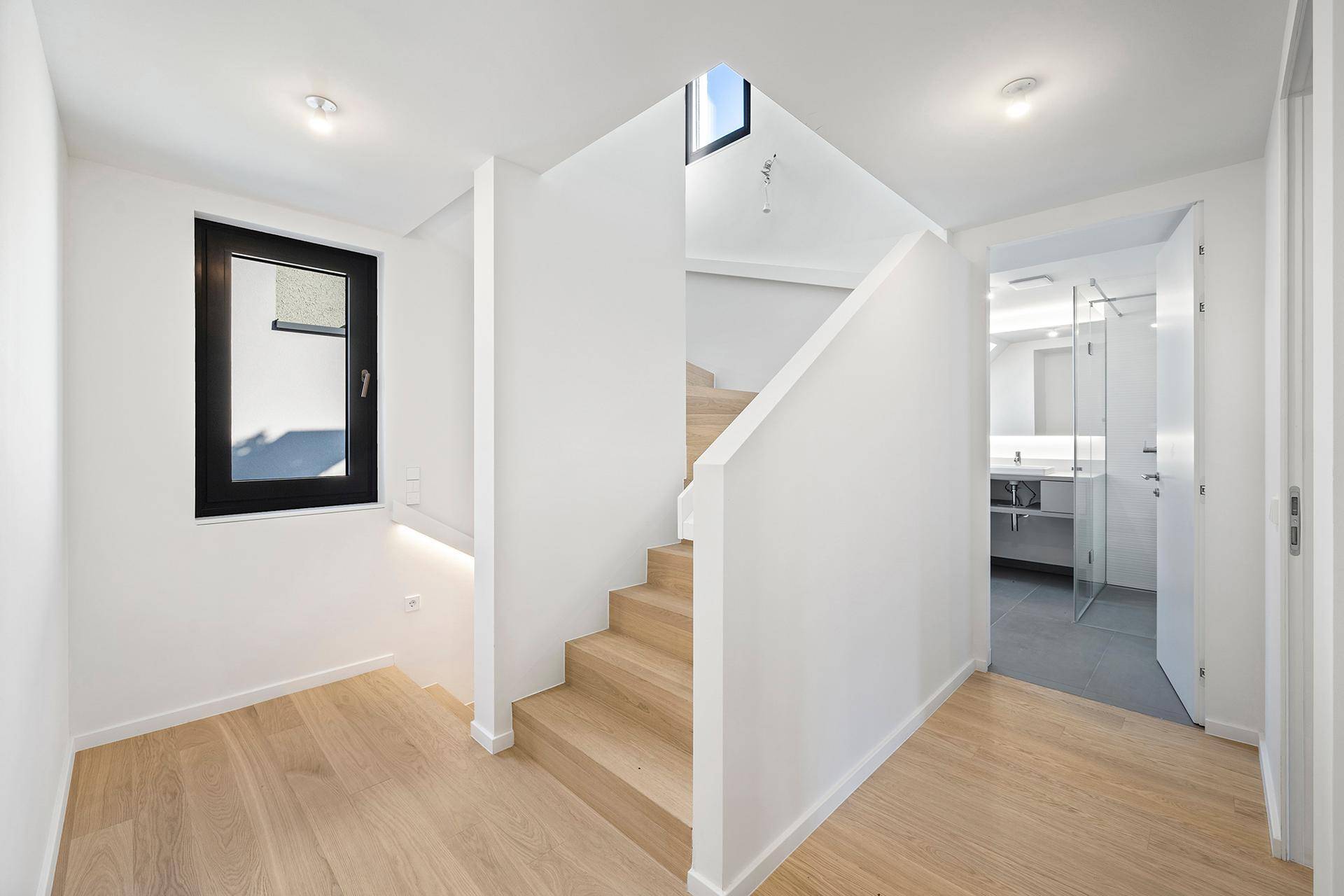 Heller Flur mit Holztreppe, Parkettboden und Zugang zu einem modernen Badezimmer.