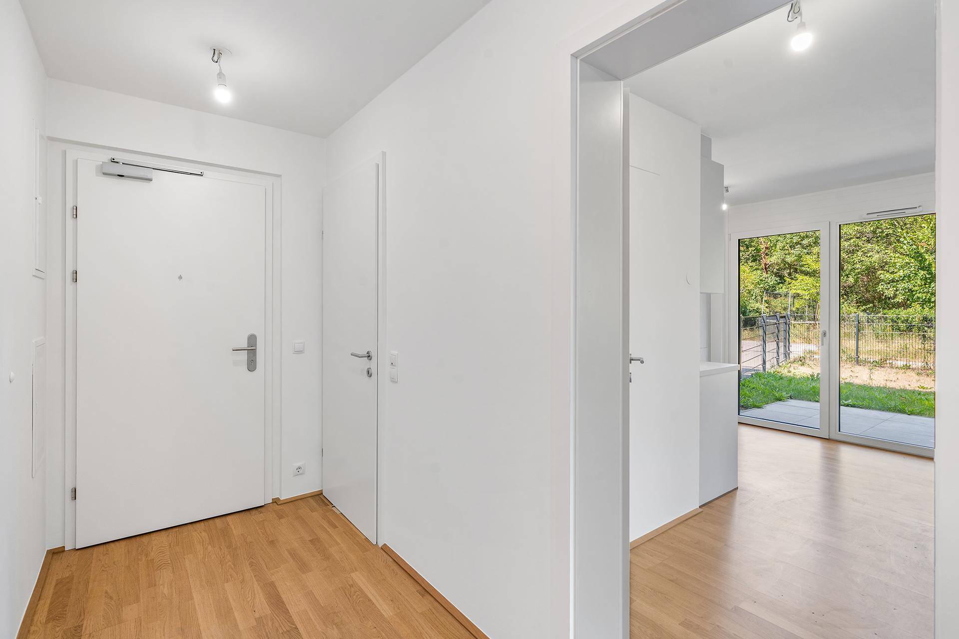 Heller Eingangsbereich mit Holzboden und weiß gestrichenen Wänden, führt in den Wohnbereich.
