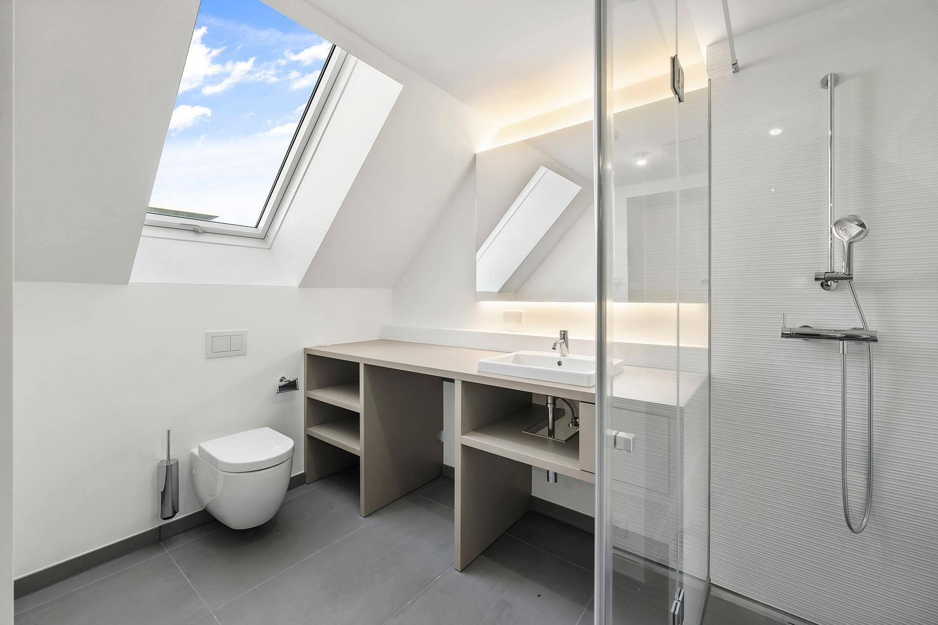 Modernes Badezimmer im Dachgeschoss mit großer Dusche, Waschtisch und Dachfenster für viel Tageslicht.