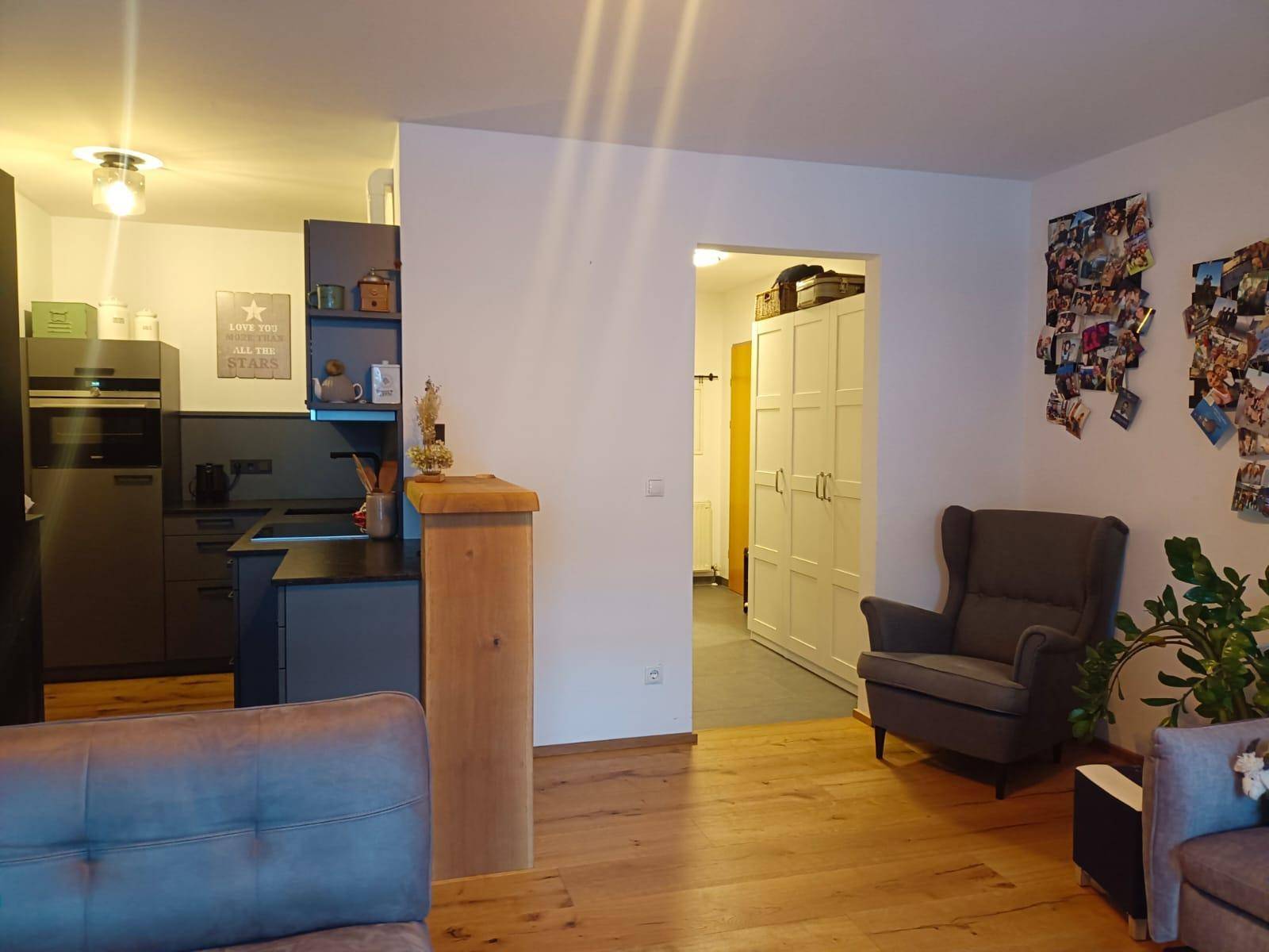 Gemütlicher Wohnbereich mit Holzboden, Sessel und Blick in die angrenzende Küche.