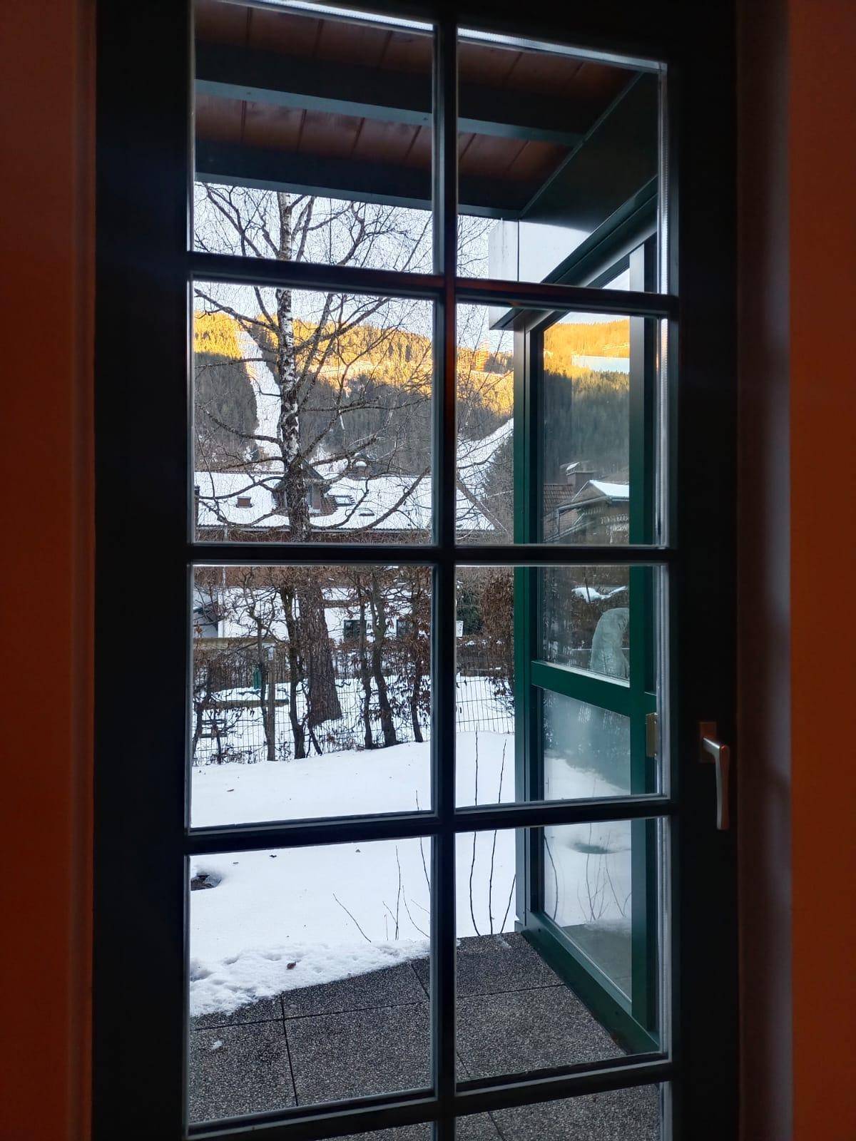 Fenster mit Blick auf die schneebedeckte Landschaft und die umliegenden Häuser im Winter.