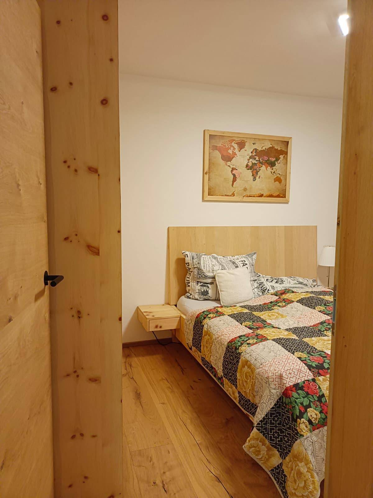 Schlafzimmer mit Holzboden, Holztür und einem Weltkartenbild an der Wand.