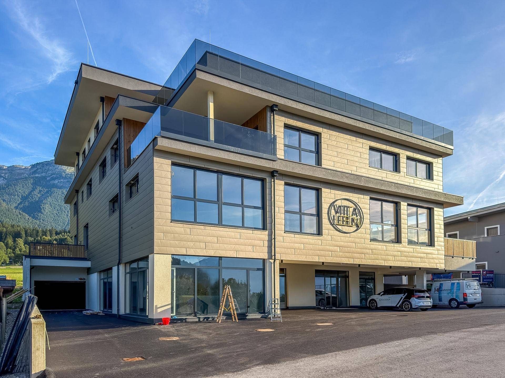 Ansicht des modernen Neubaus mit großen Fensterfronten und Parkplätzen vor dem Gebäude.