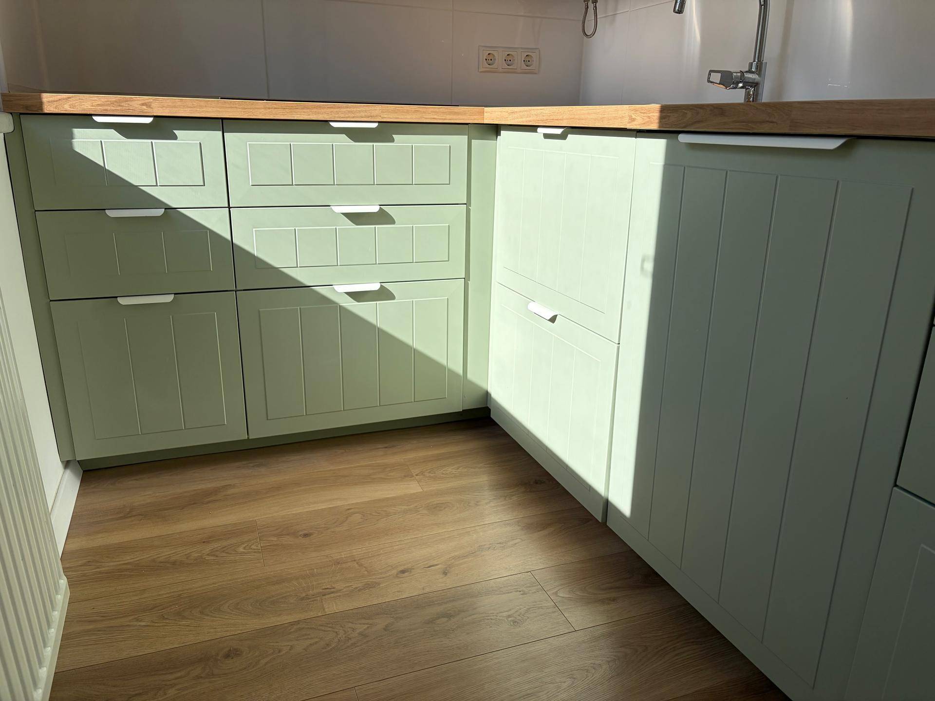 Moderne Küche mit hellgrünen Schrankfronten, Holz-Arbeitsplatte und Laminatboden.