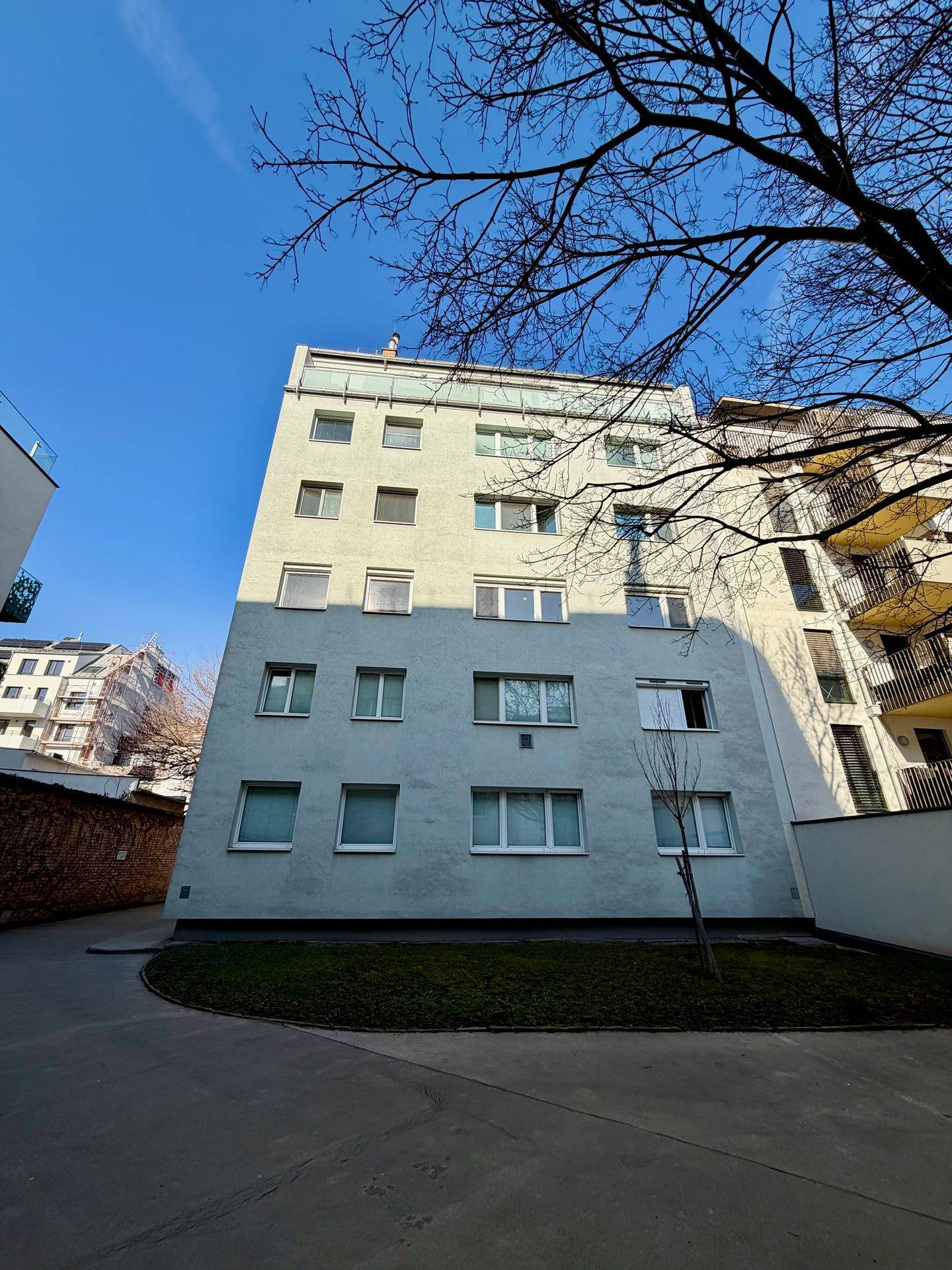 Mehrstöckiges Wohngebäude mit hellgrüner Fassade und zahlreichen Fenstern unter blauem Himmel.