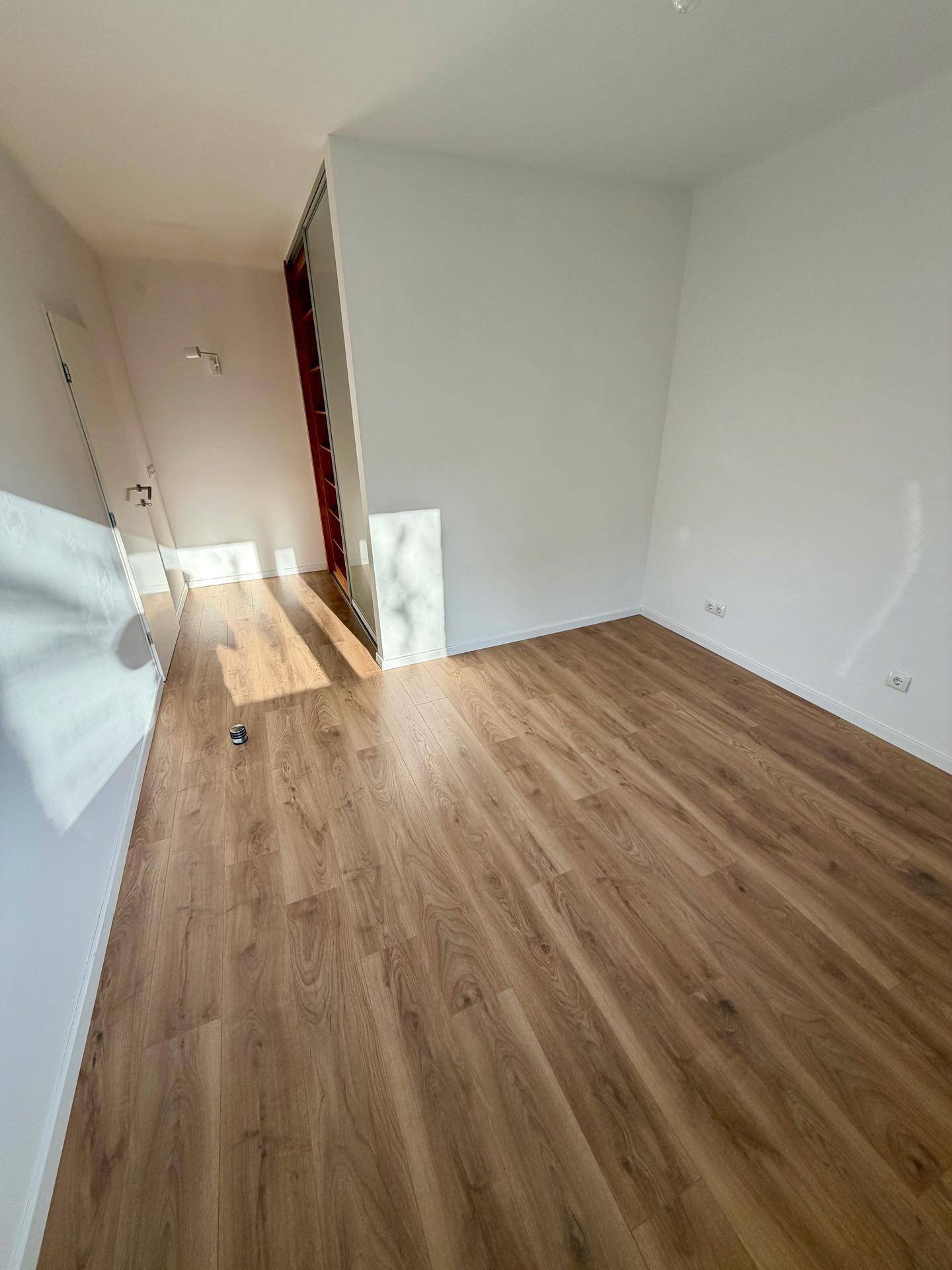 Leeres Schlafzimmer mit Laminatboden und weißen Wänden, angrenzend an einen begehbaren Kleiderschrank.