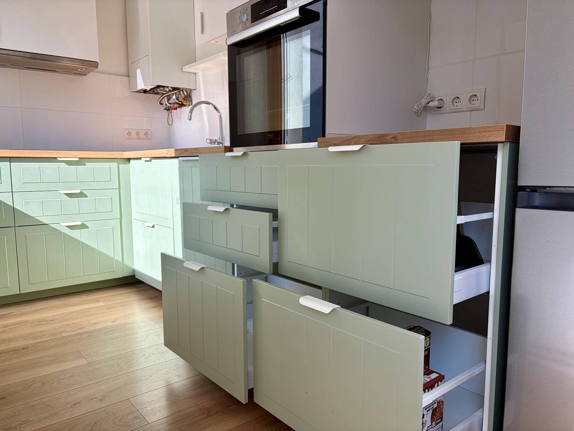 Moderne Küche mit hellgrünen Schrankfronten, Holz-Arbeitsplatte und integriertem Backofen.