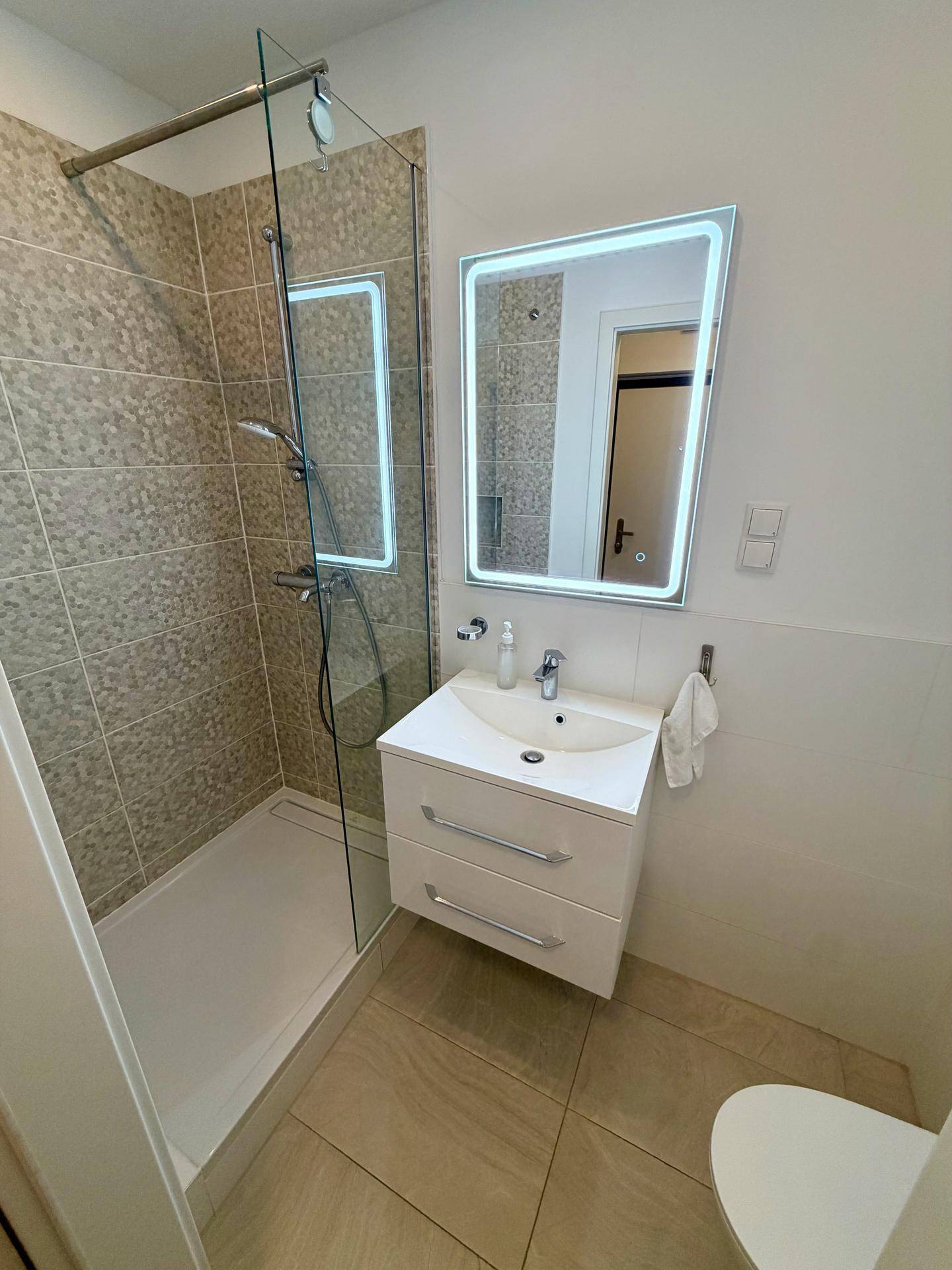 Modernes Badezimmer mit Duschkabine, Waschtisch und beleuchtetem Spiegel.
