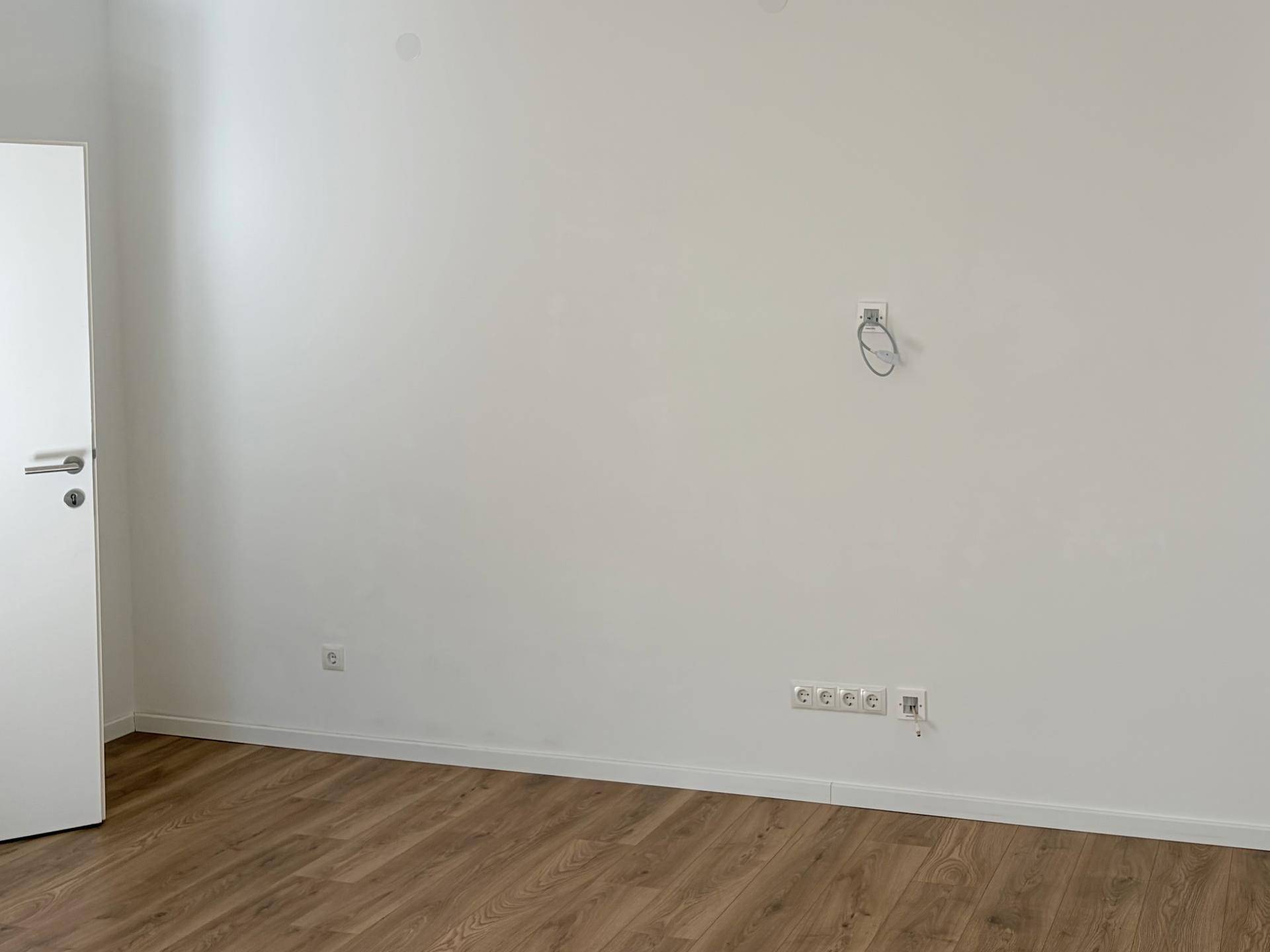 Leerer Raum mit Laminatboden und weißen Wänden, bereit für individuelle Gestaltung.