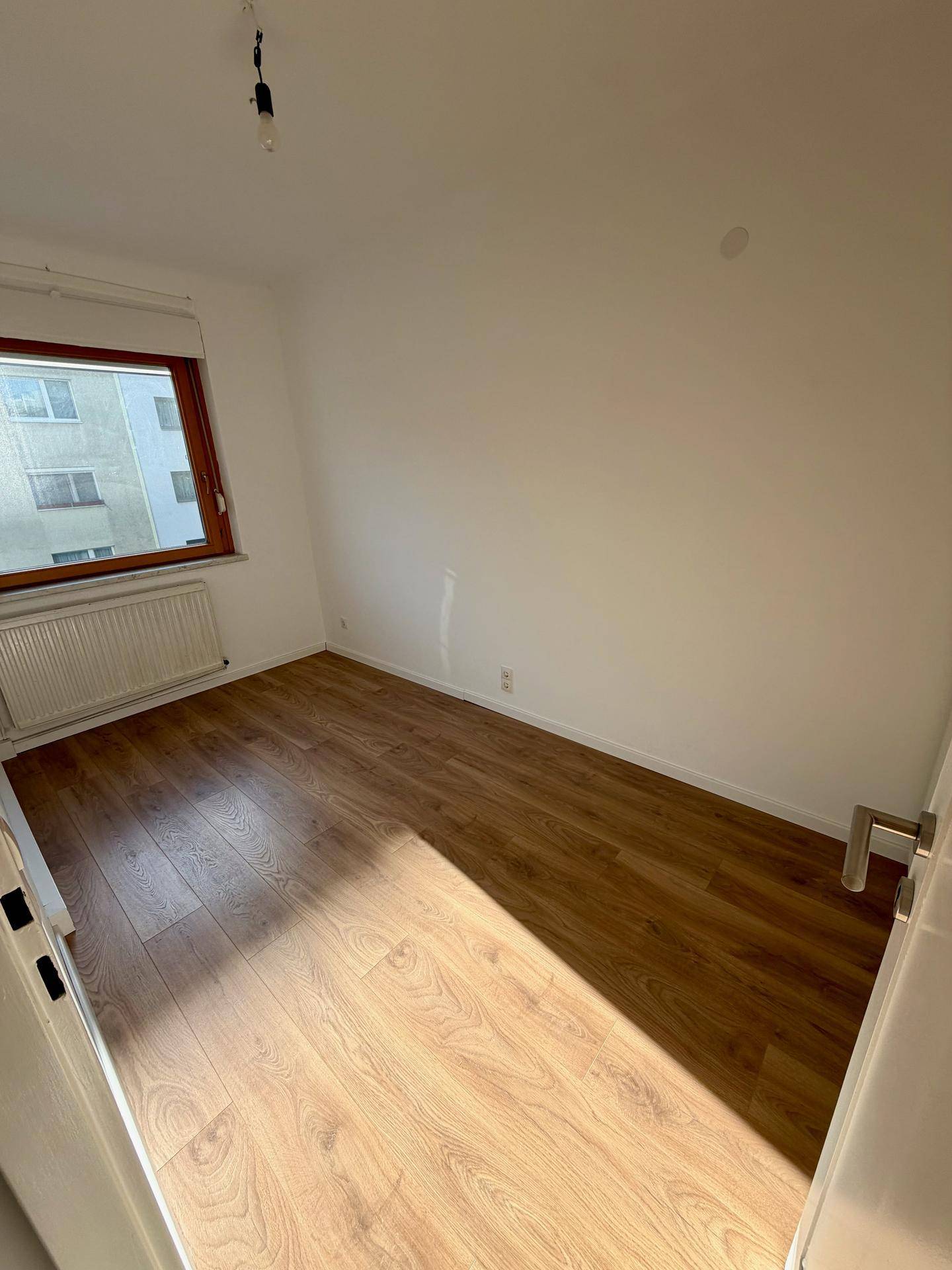 Helles leeres Zimmer mit Laminatboden und Fenster, ideal als Schlaf- oder Kinderzimmer.