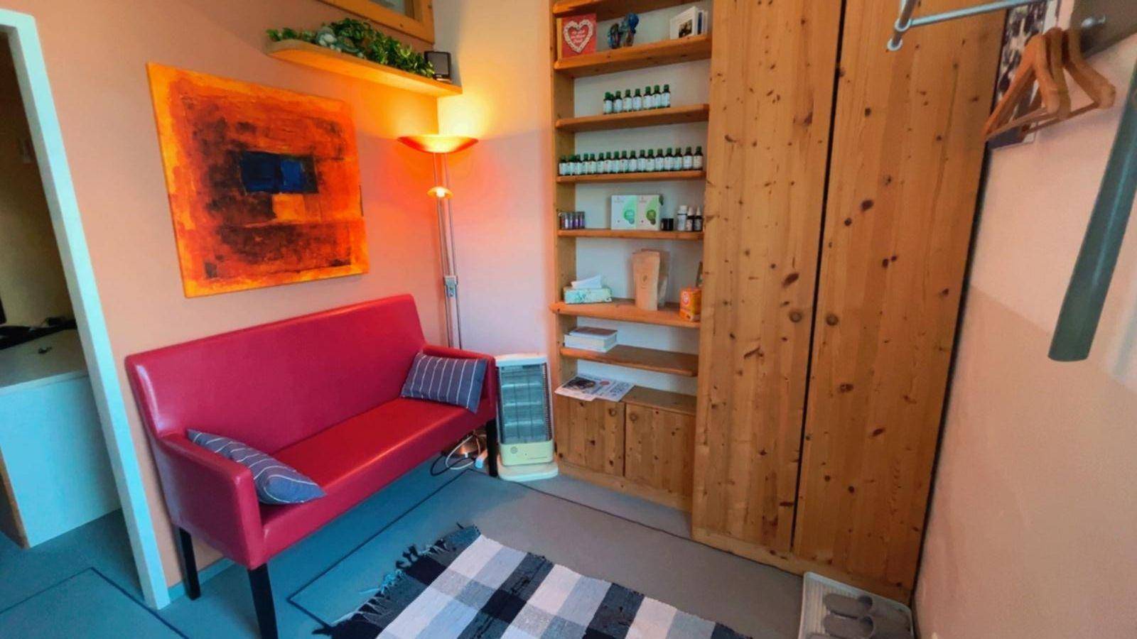 Gemütlicher Wartebereich mit rotem Sofa, Holzregalen und einem Teppich auf dem Boden.