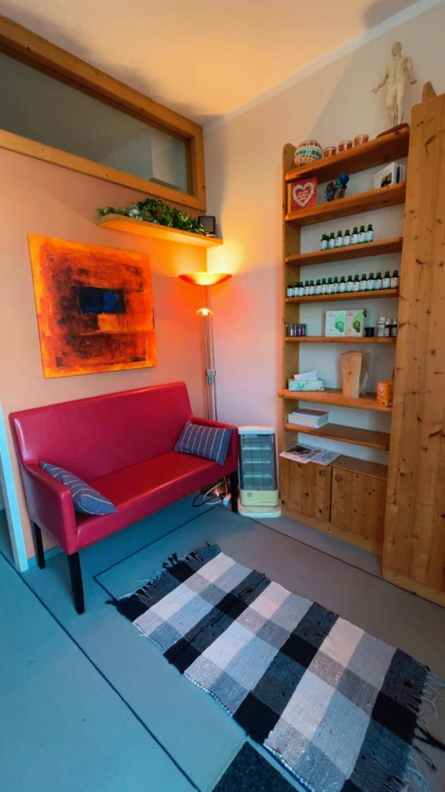 Gemütlicher Wartebereich mit rotem Sofa, Holzregalen und einem Teppich auf dem Boden.