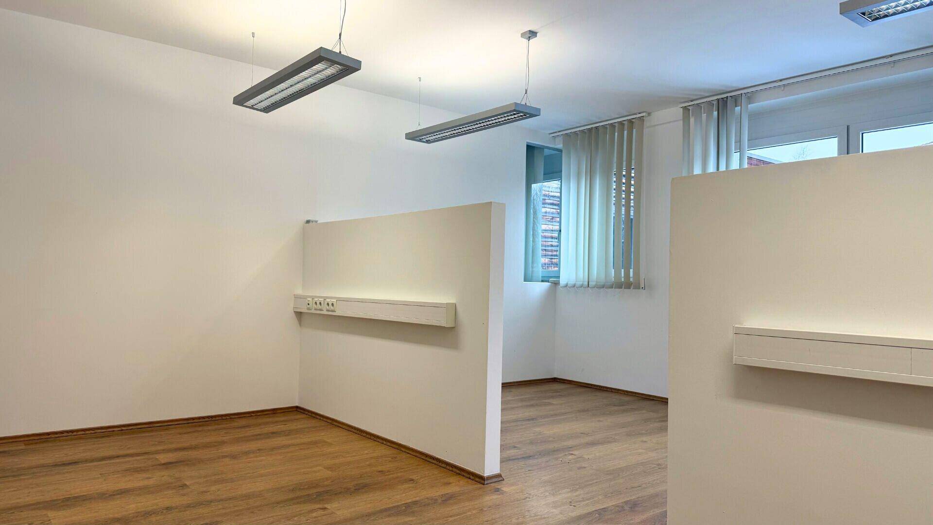 Leerer Büroraum mit Holzboden und großen Fenstern, bereit für individuelle Gestaltung.