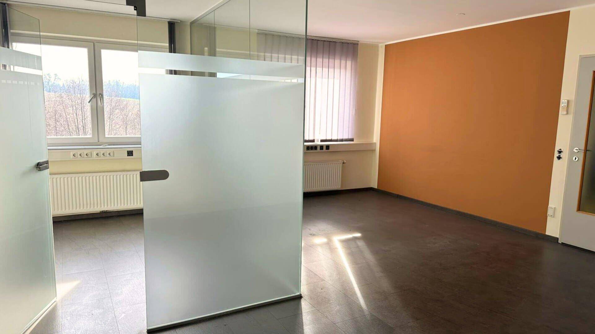 Heller Büroraum mit Glaswand und großen Fenstern, bietet viel Tageslicht und moderne Ästhetik.