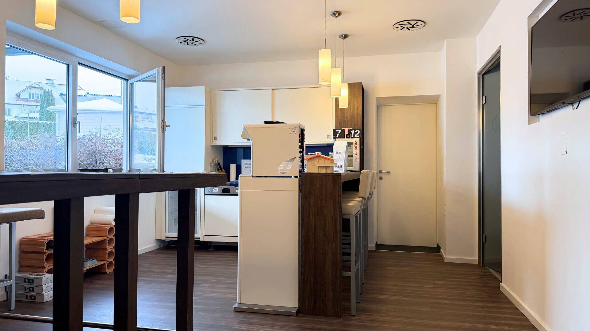 Helle Küchenzeile mit Bartheke und Hockern, ideal für Pausen, mit Blick nach draußen durch große Fenster.