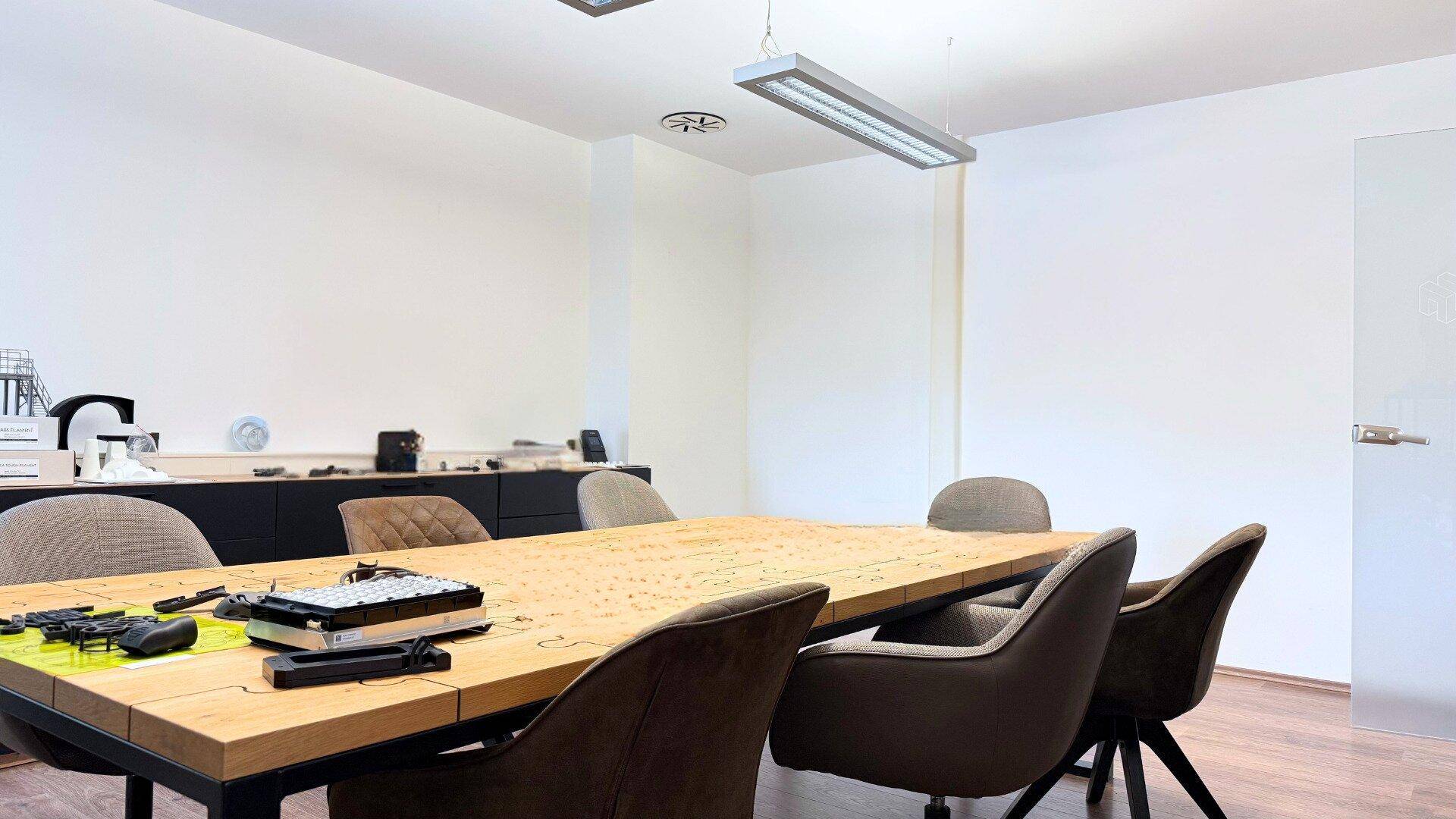 Detailansicht des Konferenztisches aus Holz mit modernen Stühlen in einem hellen und aufgeräumten Raum.