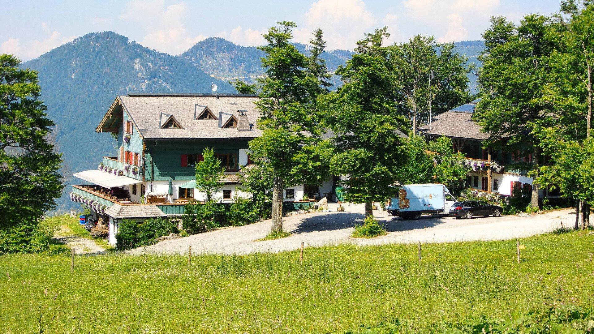 Traditionelles Gebäude mit grüner Fassade, roten Fensterläden und Balkonen in alpiner Landschaft.