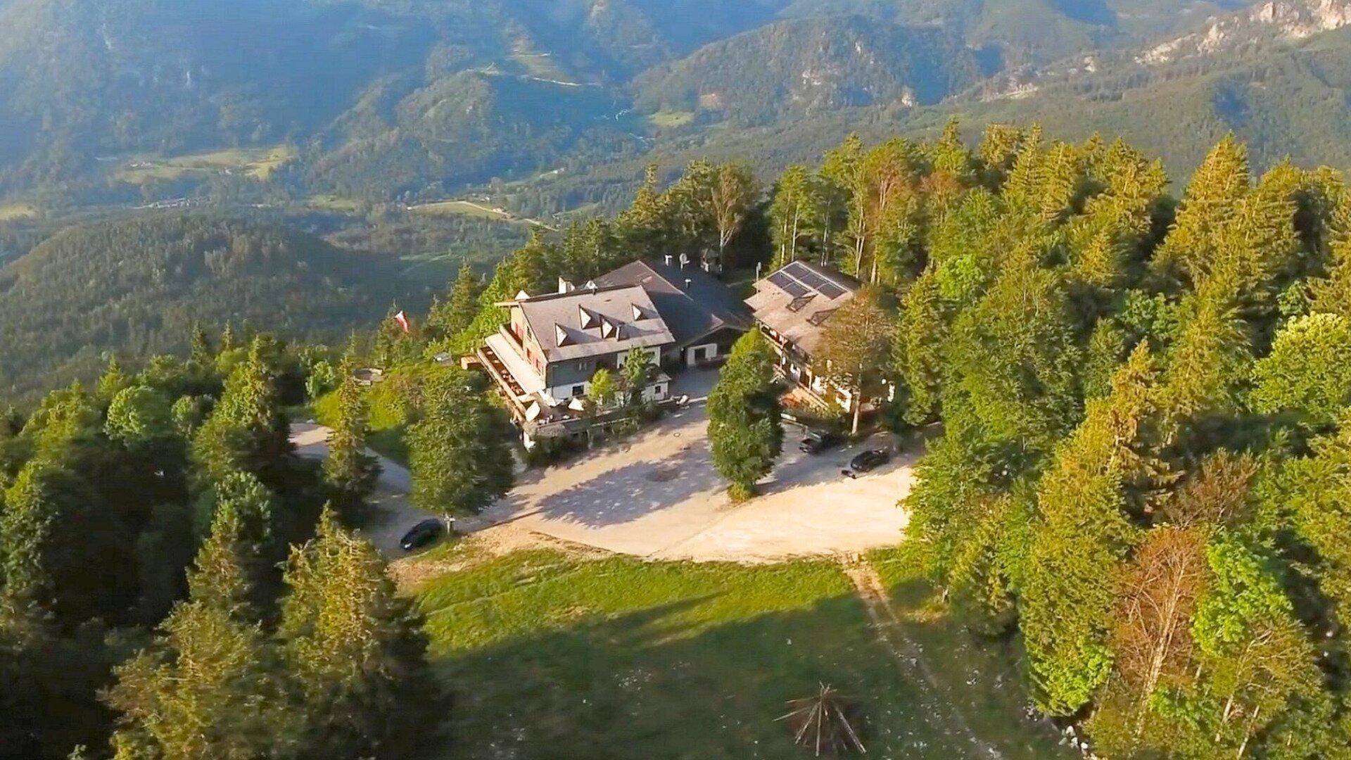 Luftaufnahme eines Gebäudekomplexes inmitten grüner Wälder und Berge mit weitem Ausblick.