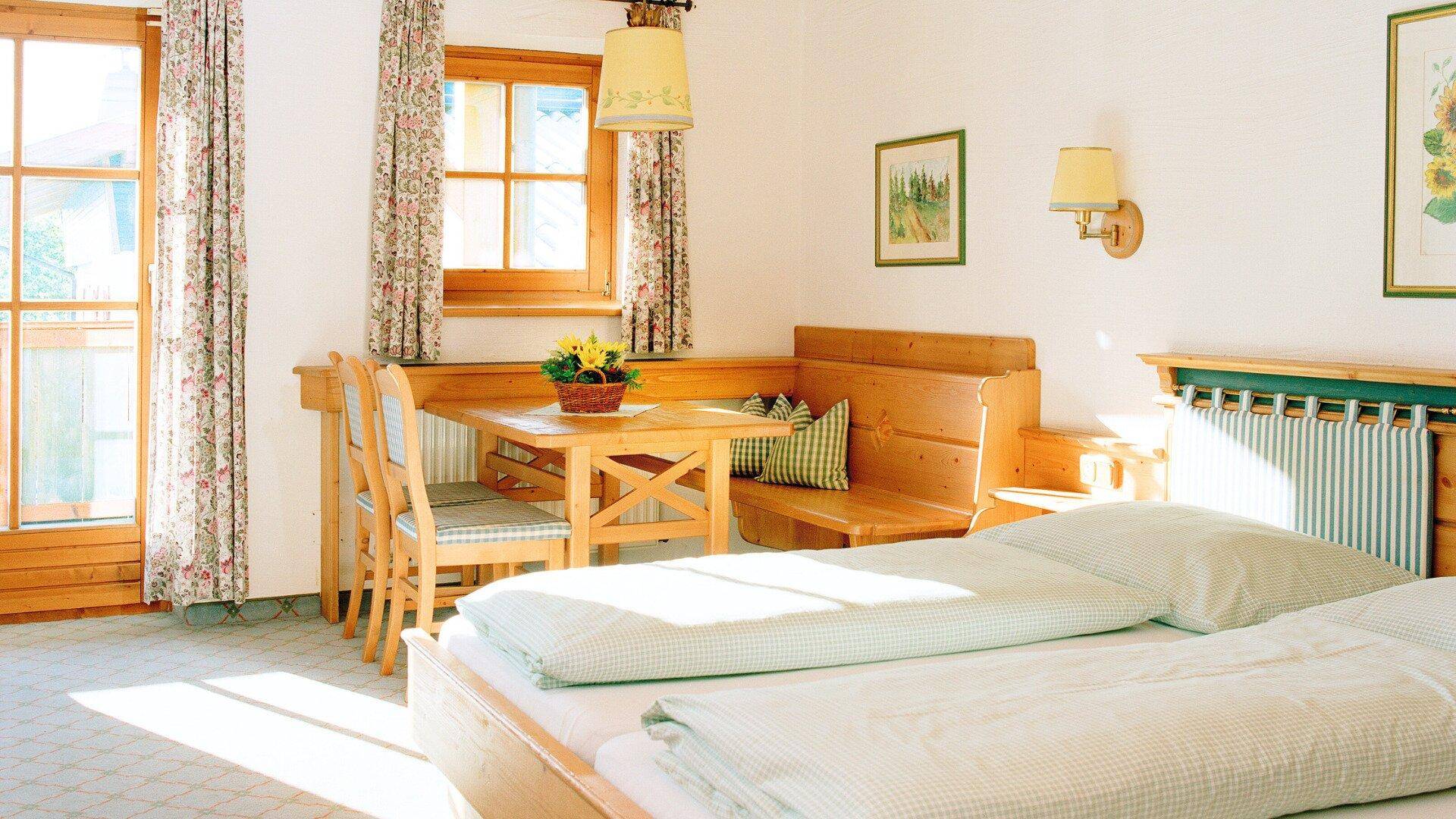 Helles Schlafzimmer mit zwei Einzelbetten, gemütlicher Sitzecke und Holzmöbeln im Landhausstil.