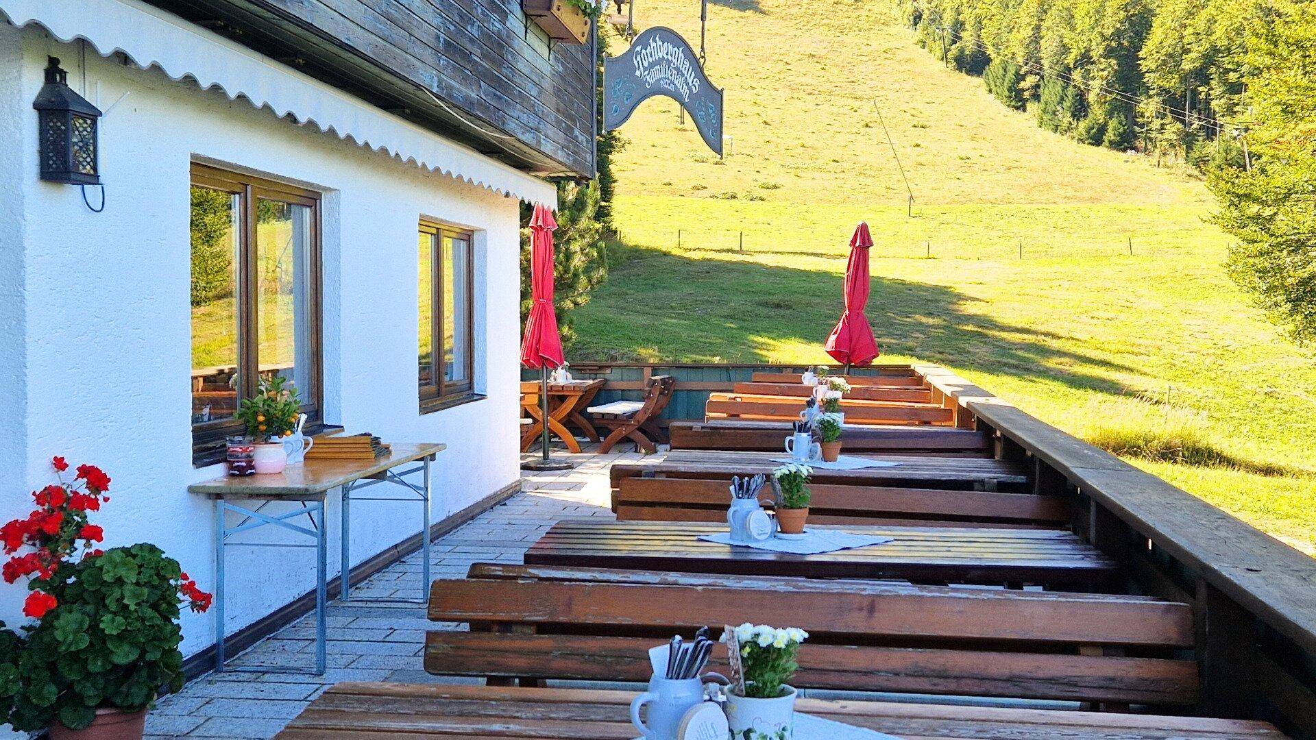 Große Sonnenterrasse mit rustikalen Holzbänken und Tischen, umgeben von grüner Natur.
