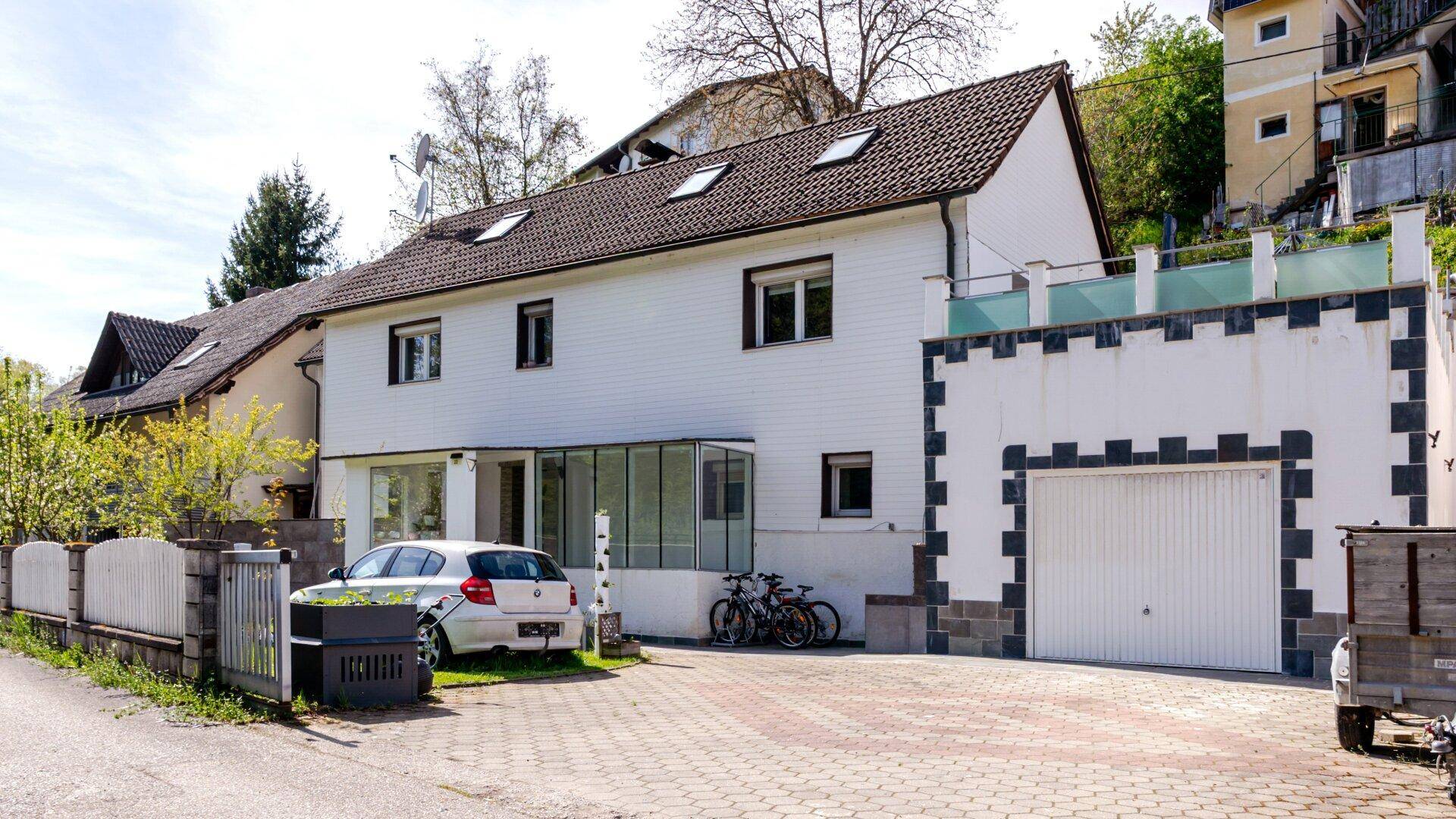 Weißes Wohnhaus mit Garage, gepflasterter Einfahrt und einem Wintergarten im Erdgeschoss.