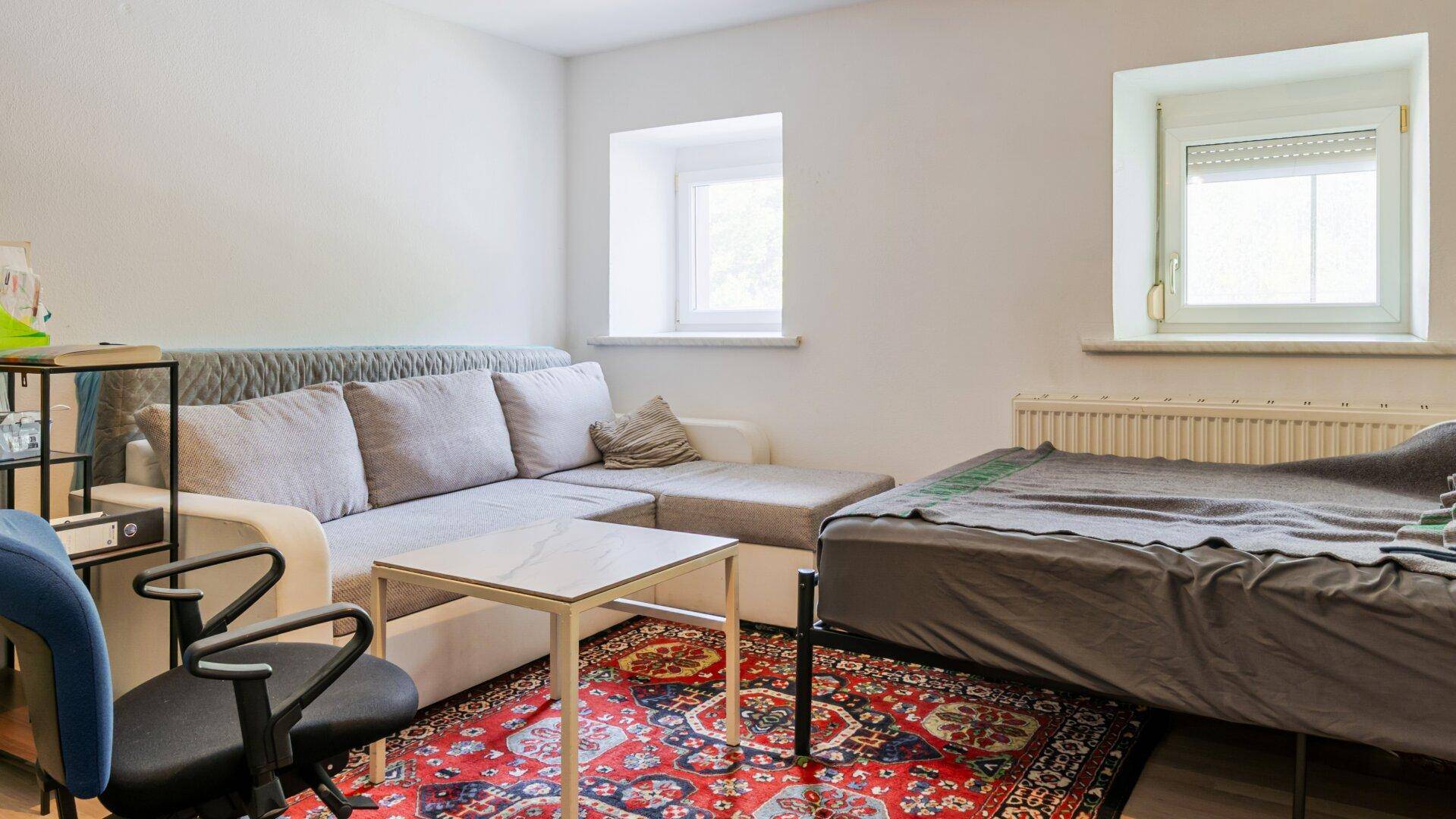Gemütliches Schlafzimmer mit Bett, Sofa und einem farbenfrohen Teppich, ideal als Gästezimmer.