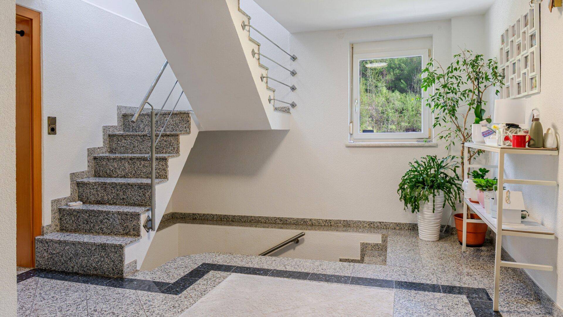 Heller Flur mit Granittreppe, gefliestem Boden und einem Fenster, das viel Licht hereinlässt.
