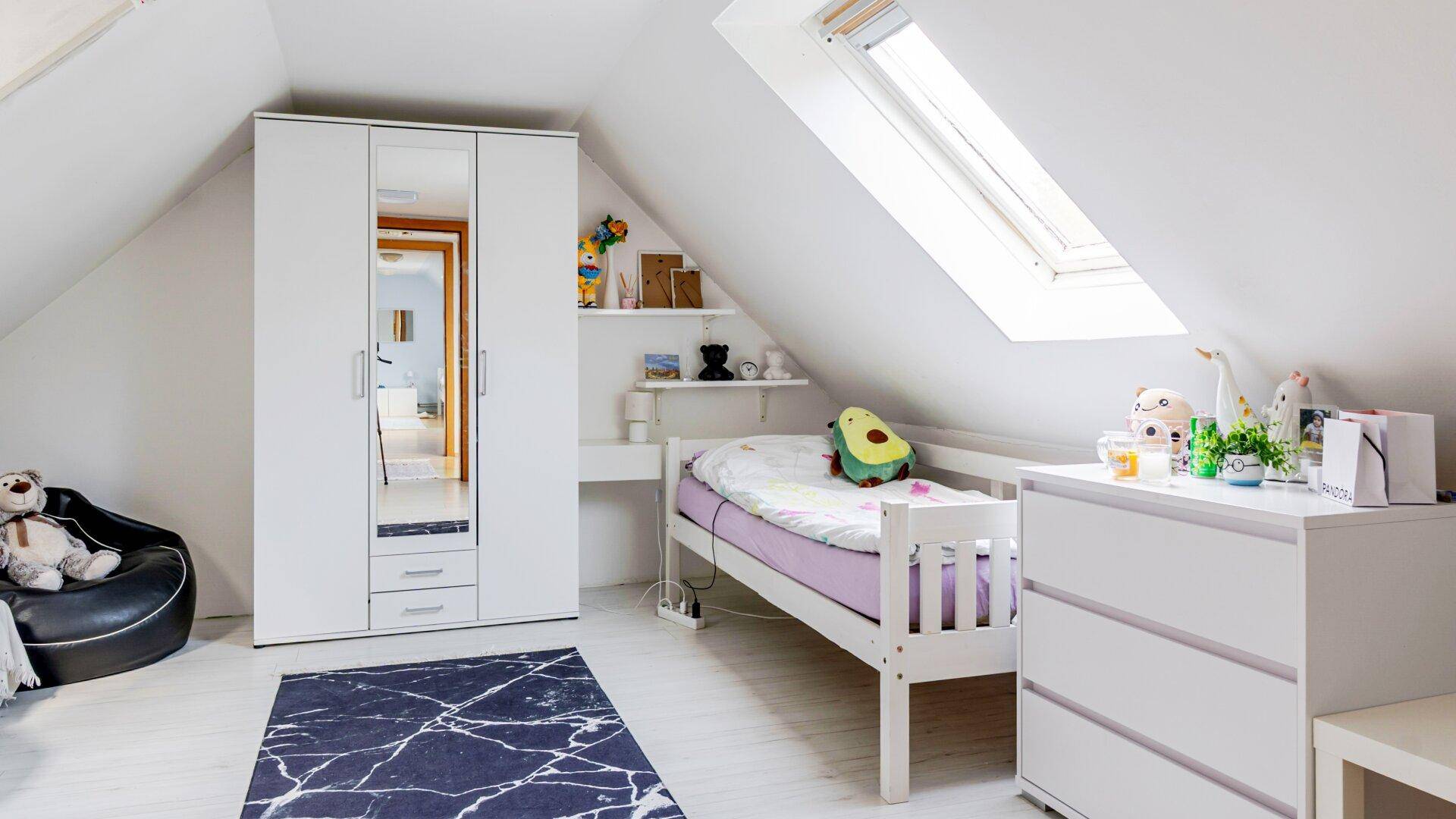 Helles Kinderzimmer im Dachgeschoss mit Einzelbett, Schrank und einem praktischen Dachfenster.