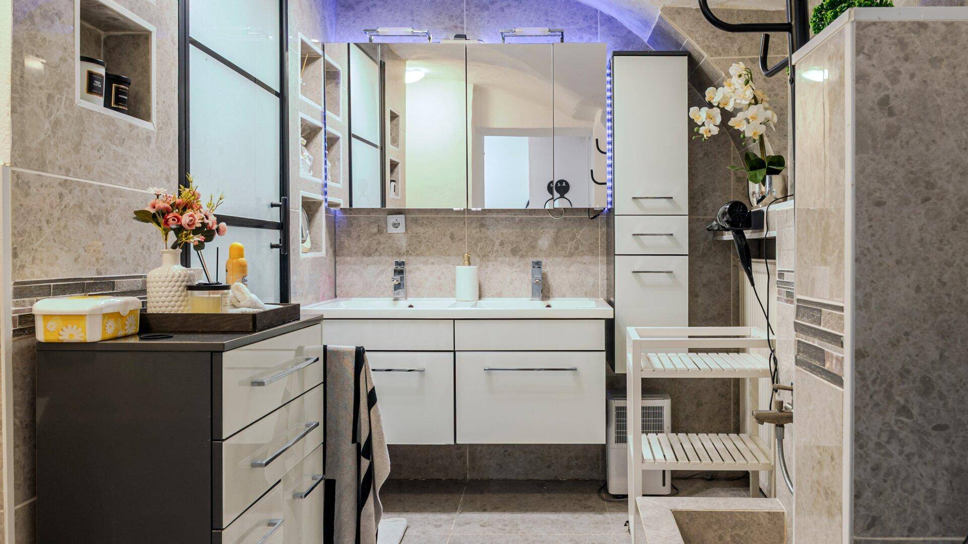 Modernes Badezimmer mit Doppelwaschbecken, großem Spiegelschrank und eleganten grauen Fliesen.