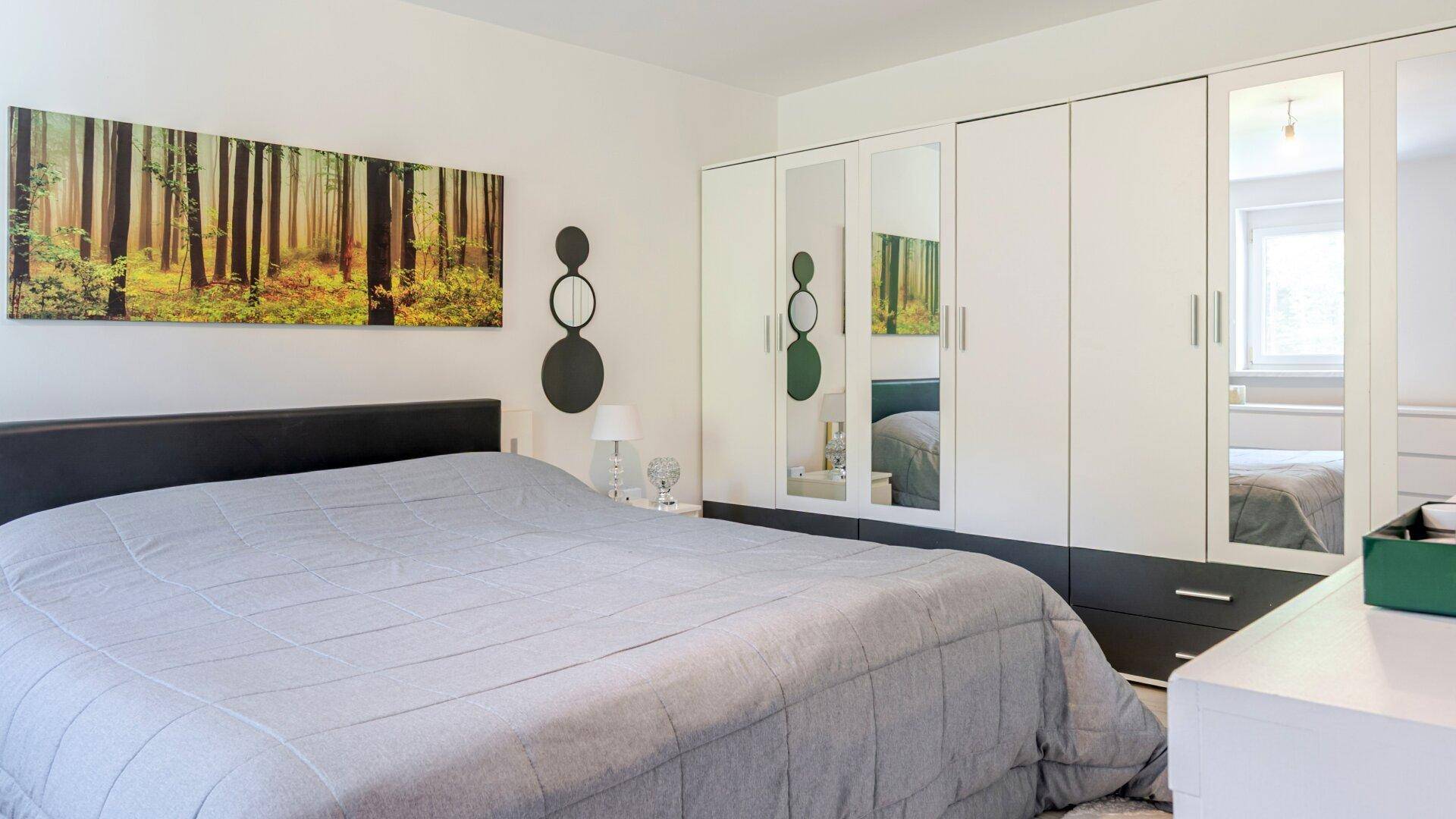 Geräumiges Schlafzimmer mit großem Bett, Spiegelschränken und einem beruhigenden Waldbild.