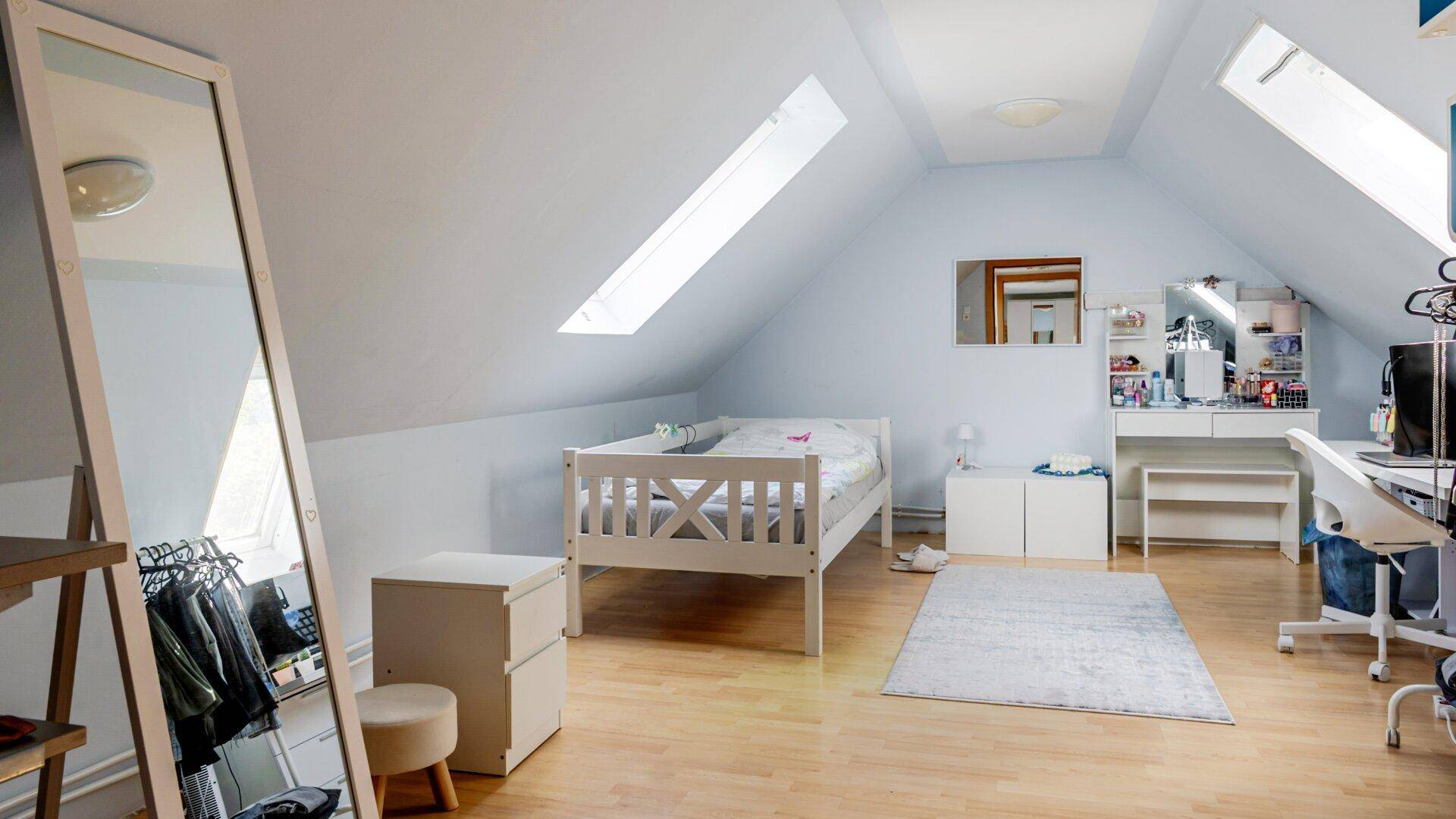 Geräumiges Dachgeschoss-Schlafzimmer mit Bett, Schreibtisch und viel natürlichem Licht durch Dachfenster.