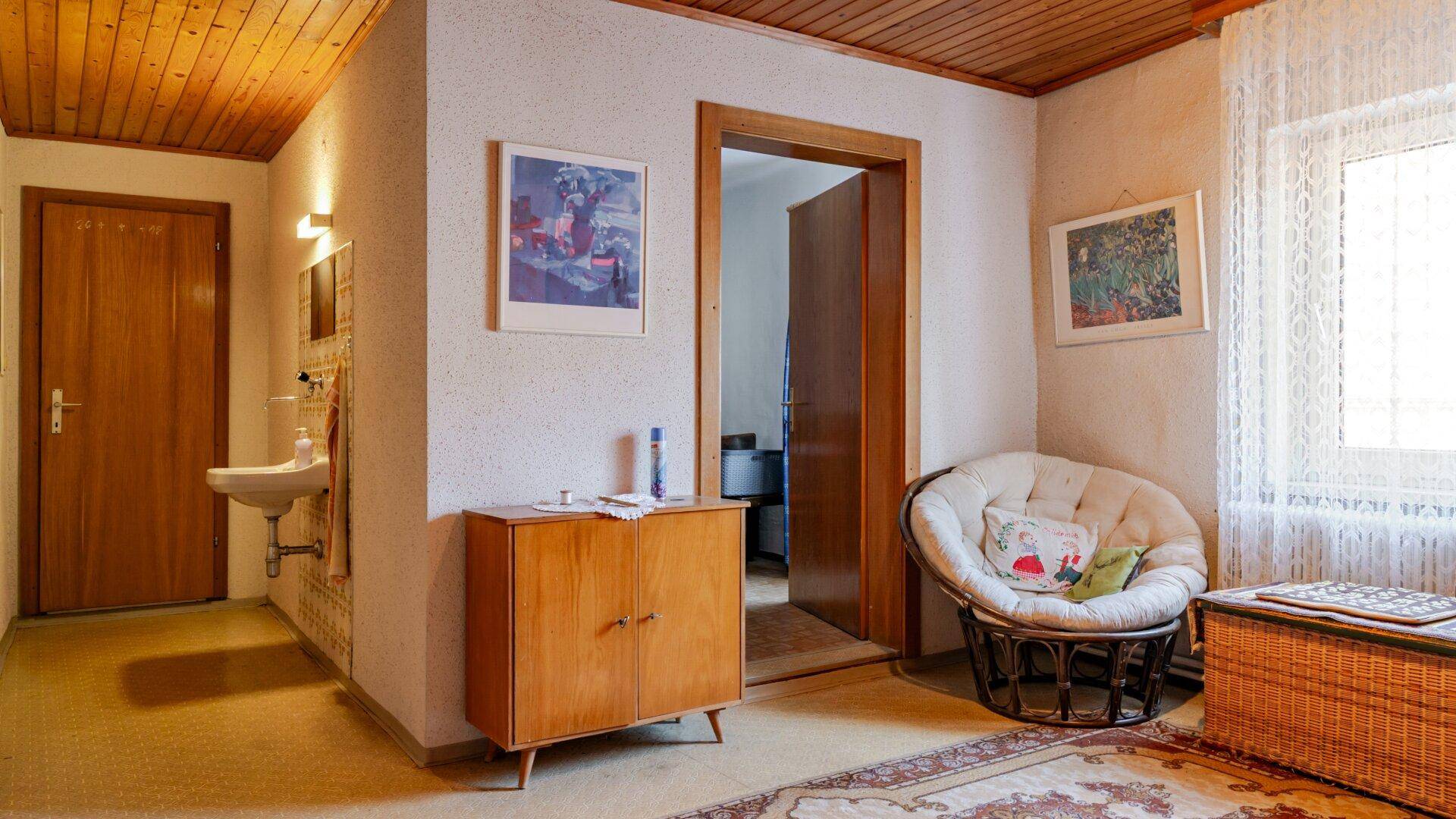 Flur mit Holzdecke, Teppichboden und einem kleinen Waschbeckenbereich.