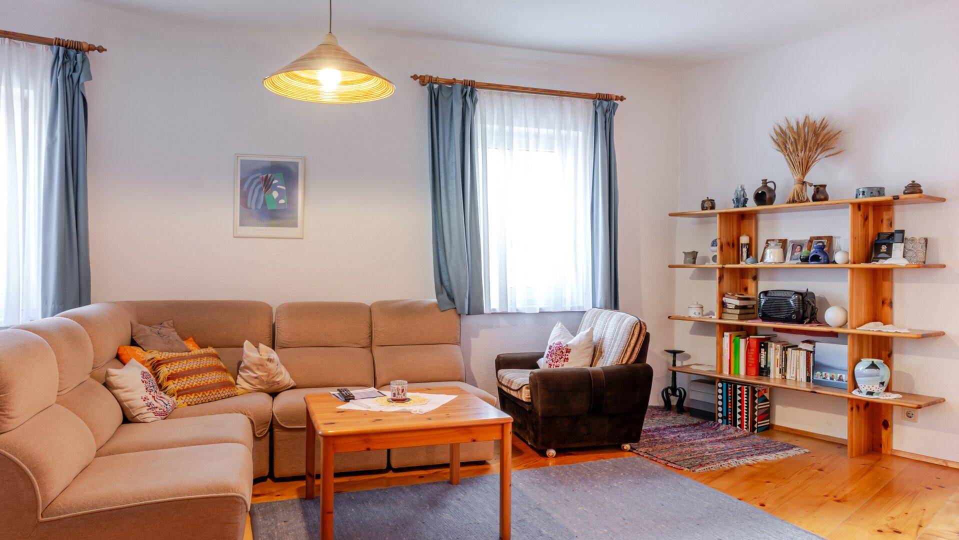 Helles Wohnzimmer mit Holzfußboden, beiger Couch und rustikalem Holzregal.