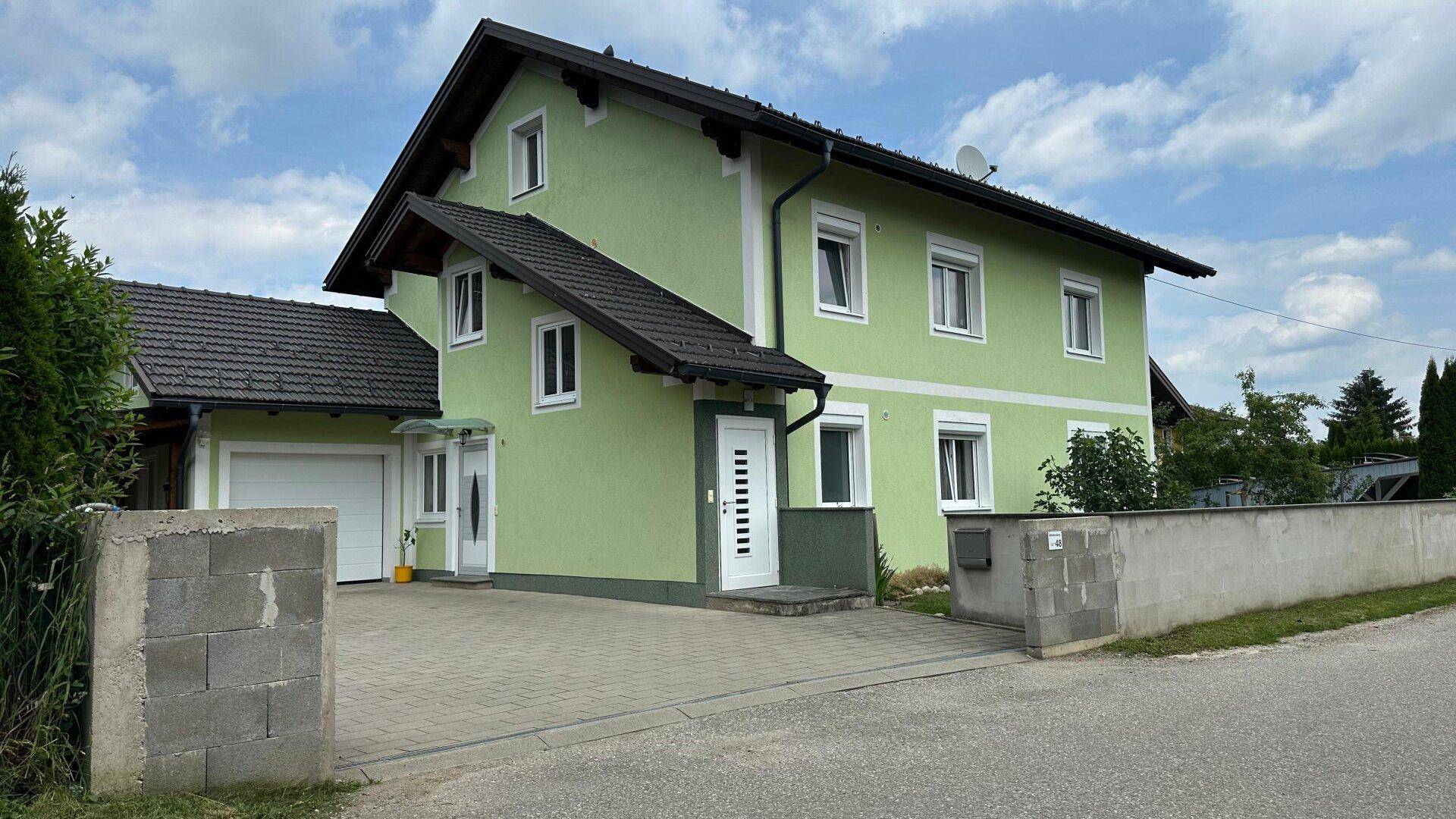 Ansicht des hellgrünen Einfamilienhauses von der Straße mit Garage und Vorgarten.