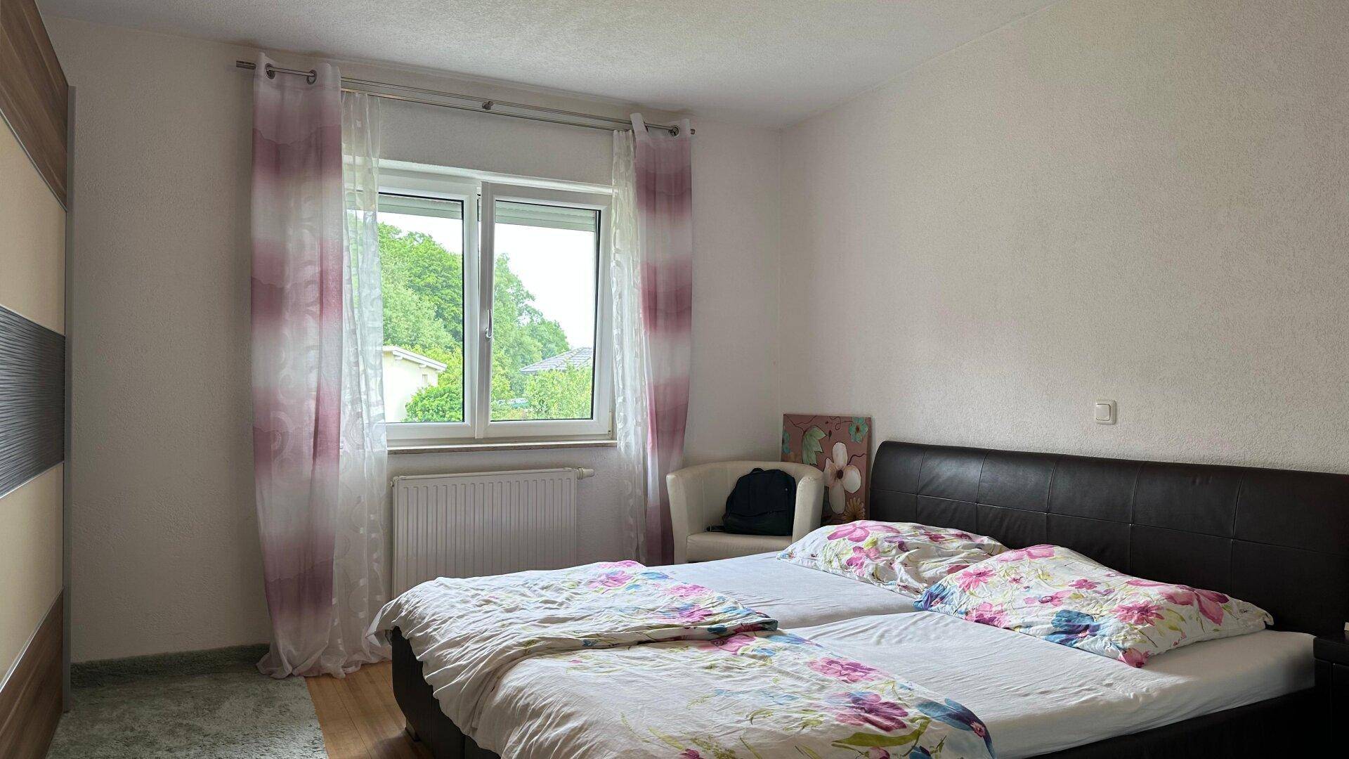 Schlafzimmer mit Doppelbett, Kleiderschrank und Fenster mit hellen Vorhängen.