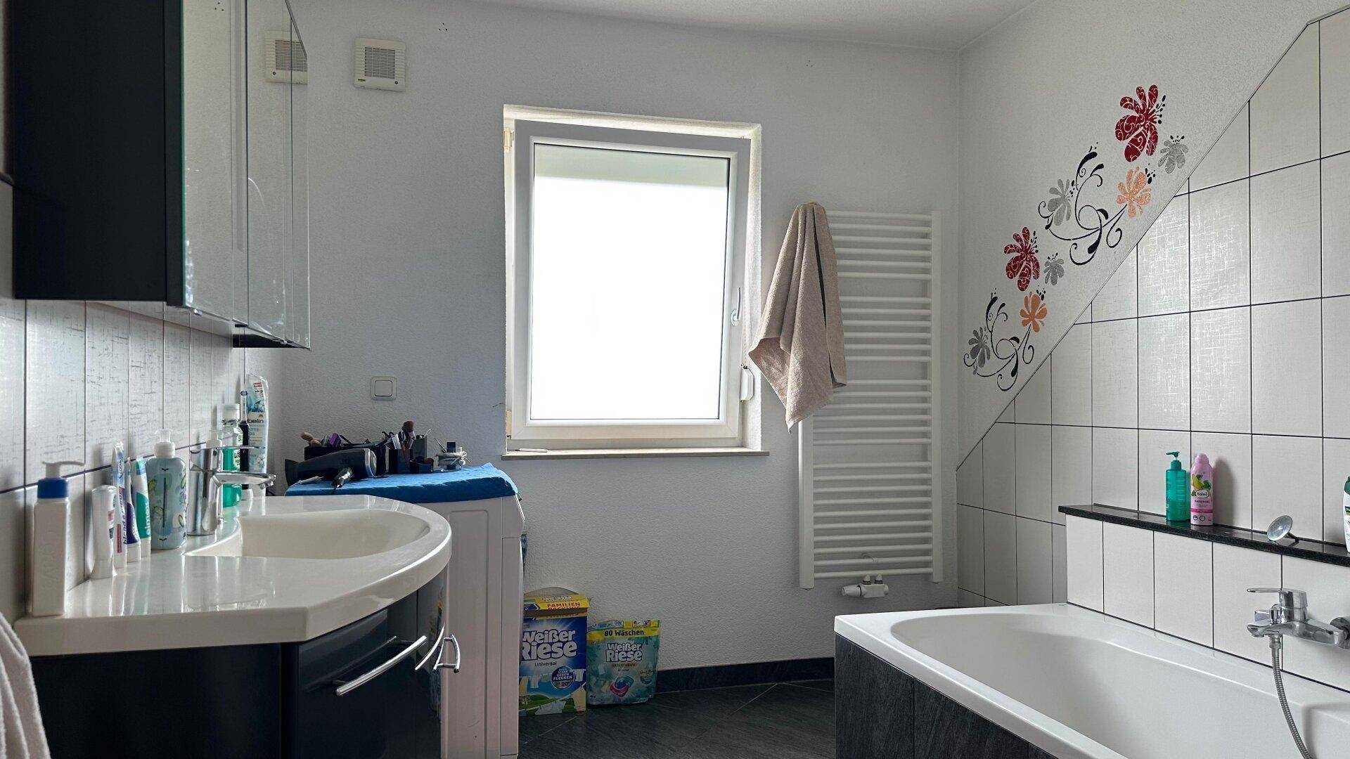 Badezimmer mit Badewanne, Waschbecken, Waschmaschine und Fenster, inklusive Handtuchheizkörper.