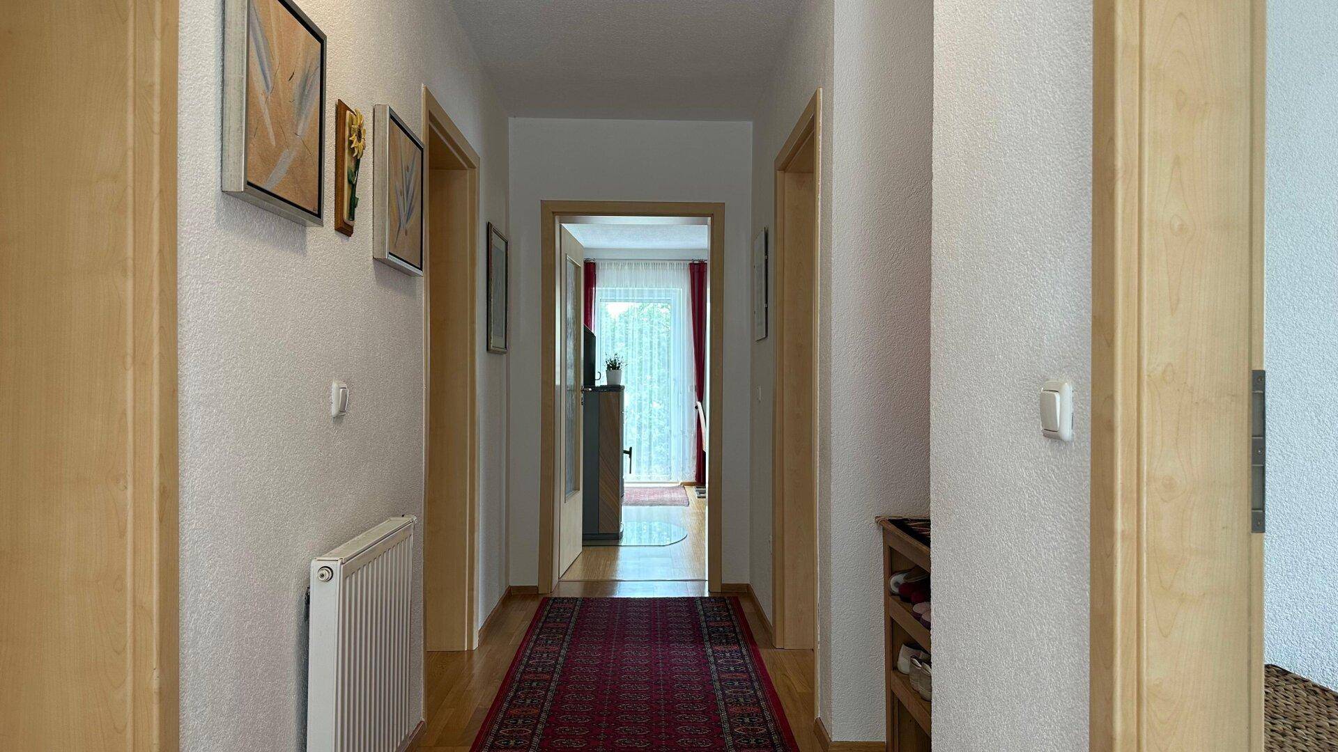 Heller Flur mit Holztüren, Teppichläufer und Bildern an den Wänden.