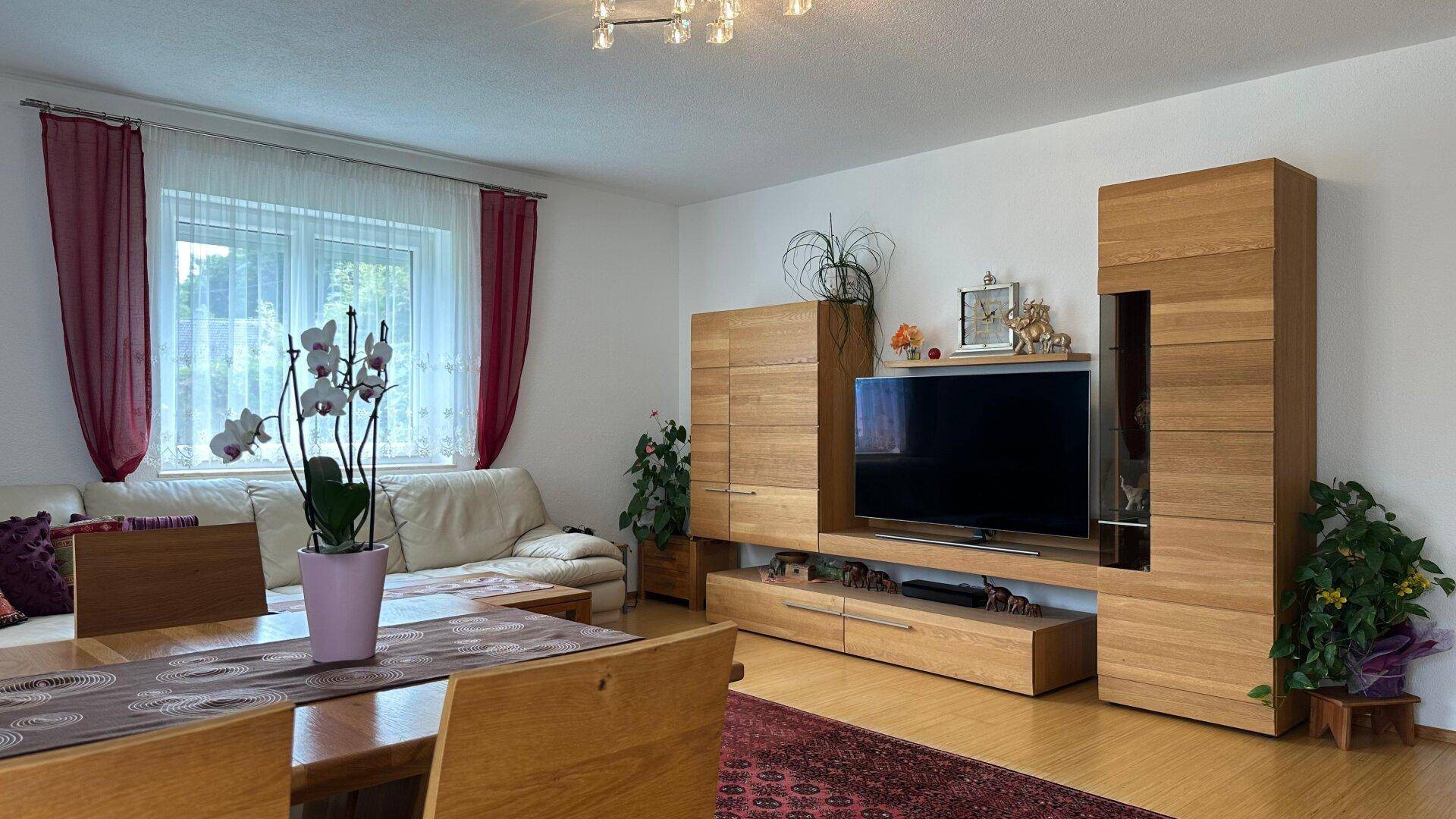 Gemütlicher Wohn-Essbereich mit heller Couch, Holzeinrichtung und einem großen Fernseher.