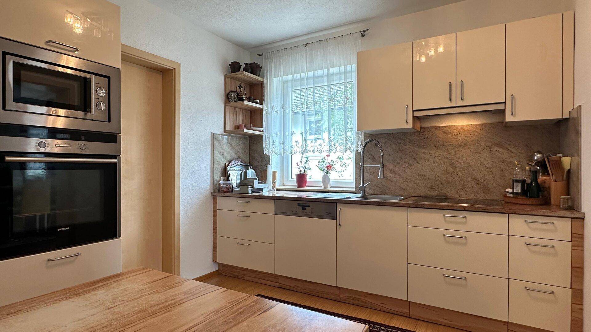 Moderne Küche mit hellen Schränken, integrierten Geräten und Fenster für natürliches Licht.