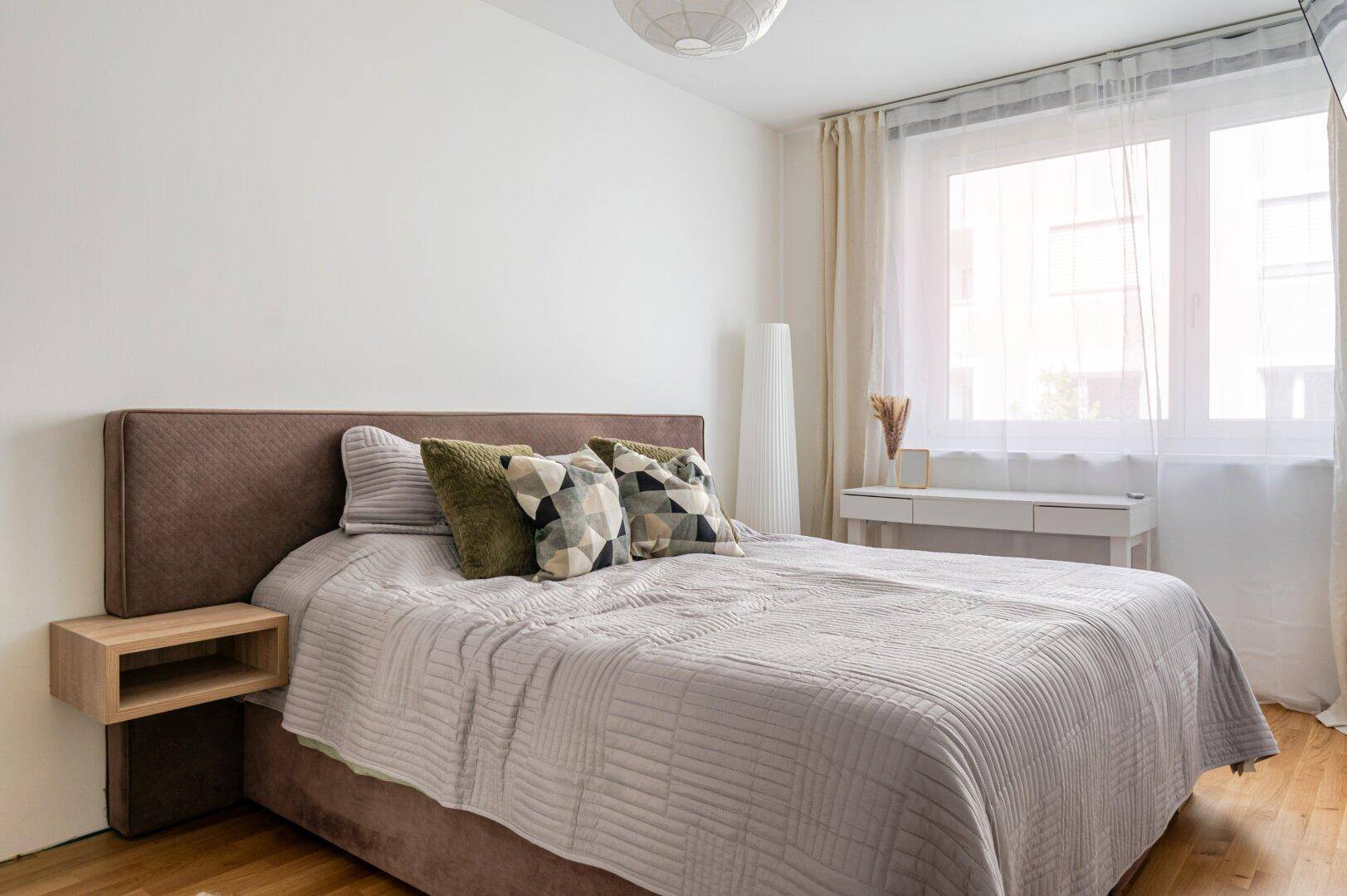 Gemütliches Schlafzimmer mit Doppelbett, Holzboden und großem Fenster für viel Tageslicht.