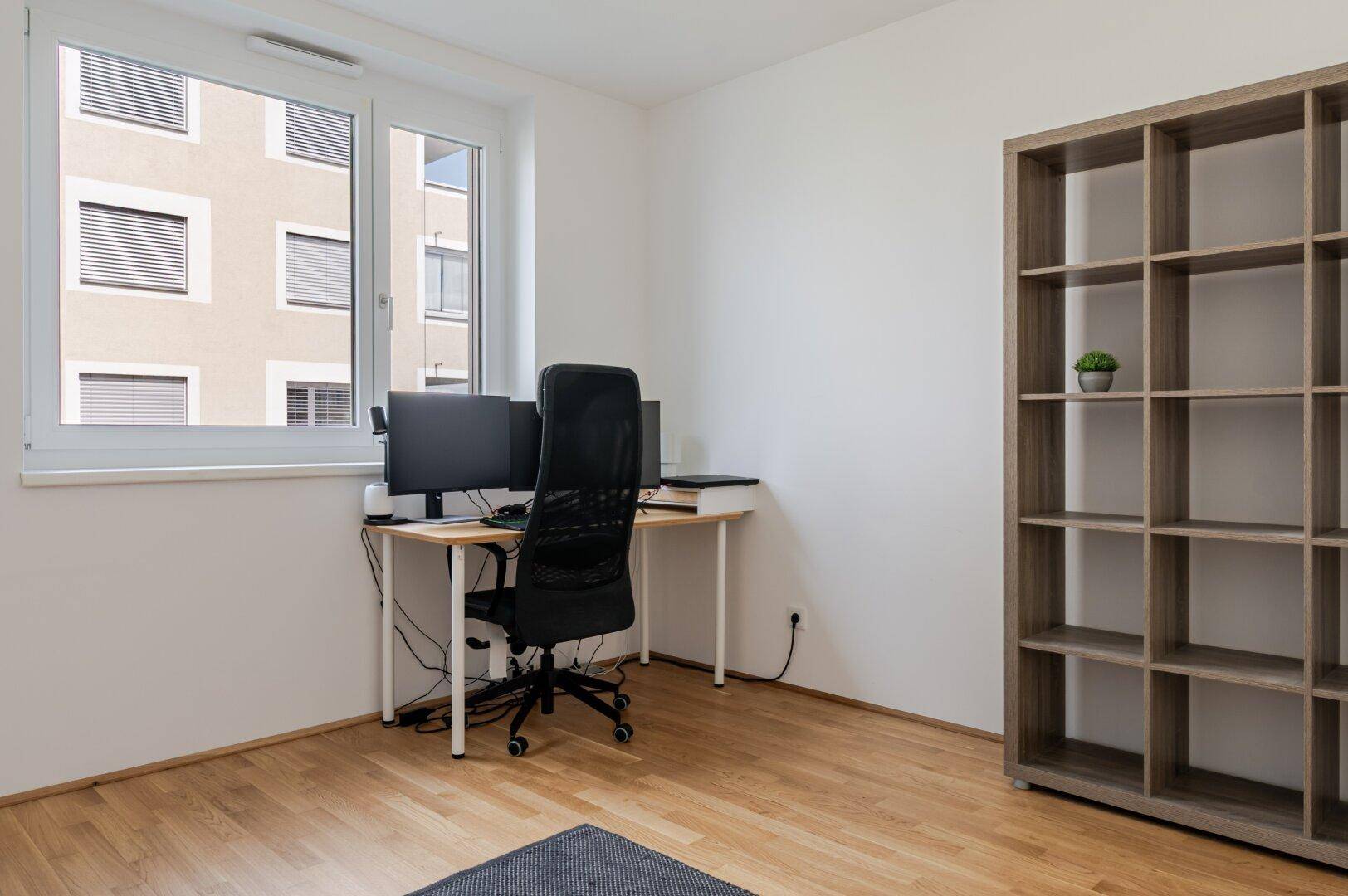 Helles Arbeitszimmer mit Schreibtisch, Bürostuhl und Regal, ideal für Home-Office-Tätigkeiten.