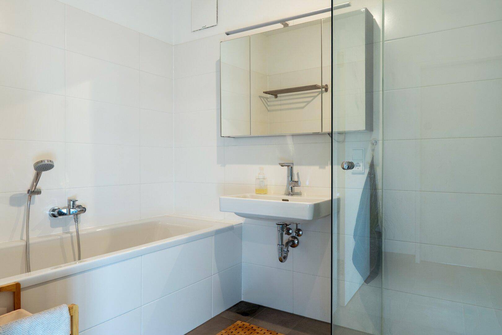 Modernes Badezimmer mit Badewanne, Waschbecken, Spiegelschrank und Duschbereich mit Glasabtrennung.
