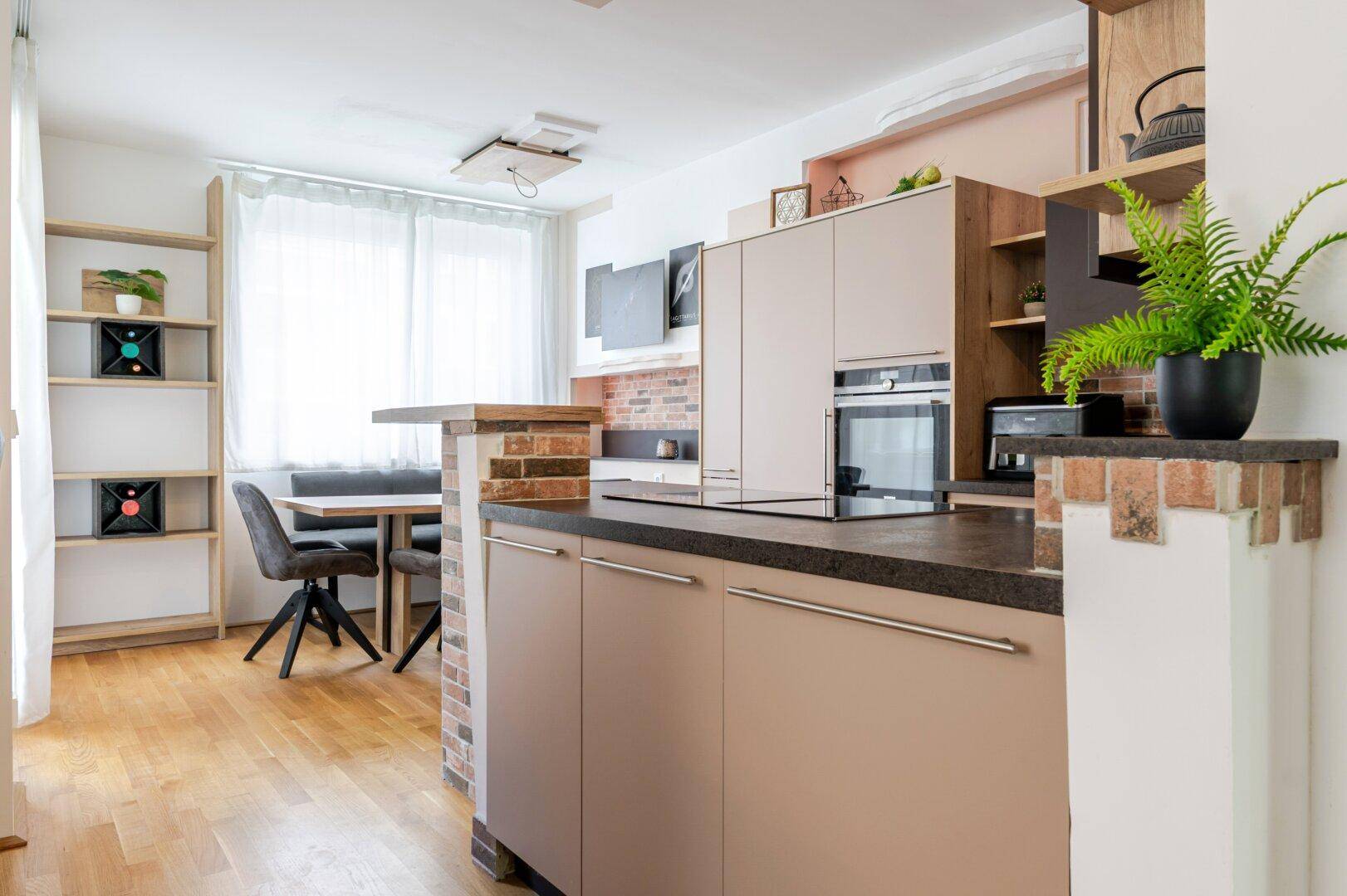 Moderne offene Küche mit hellen Schränken, dunkler Arbeitsplatte und integriertem Essbereich mit Holzboden.