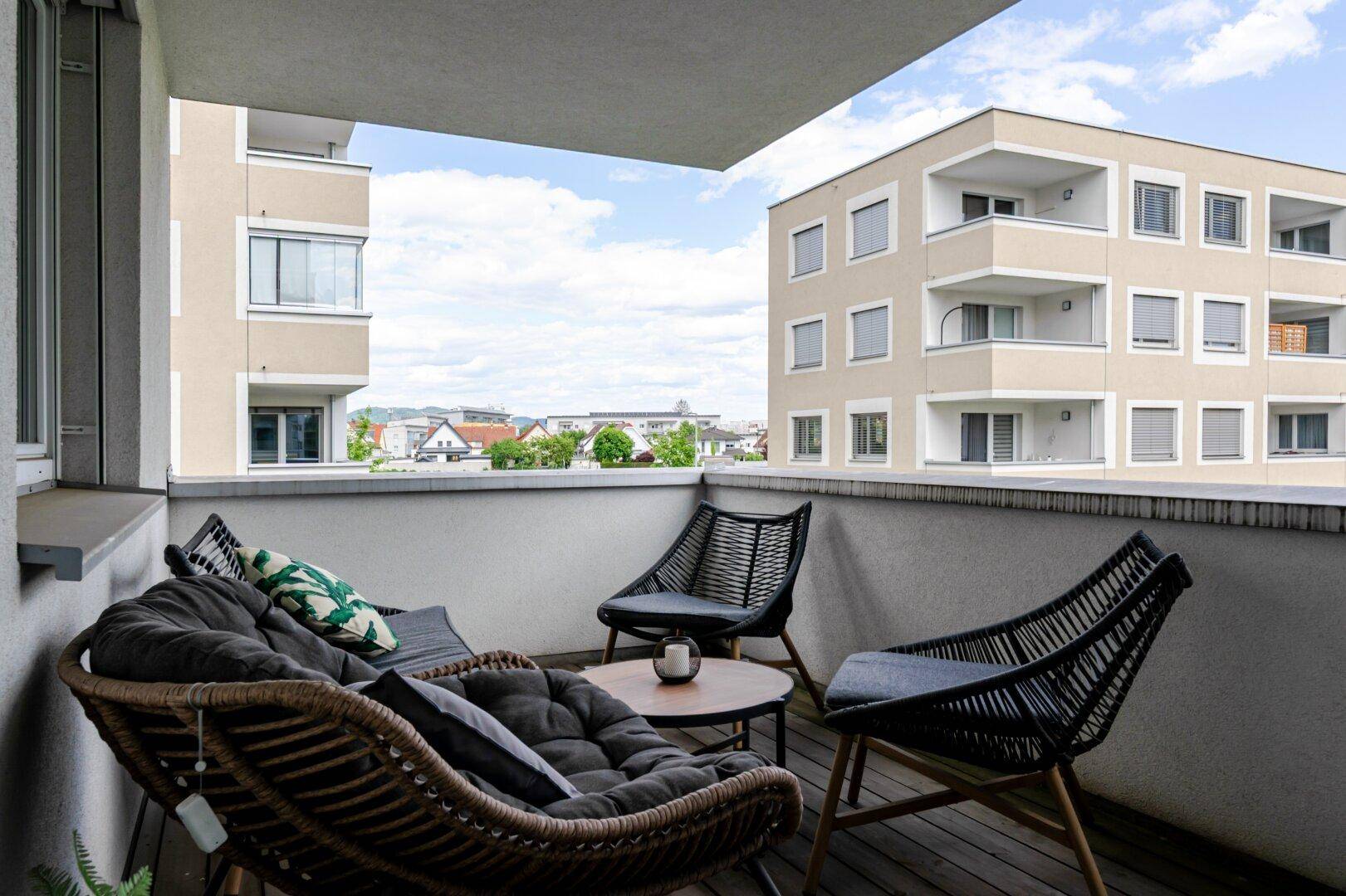 Gemütlicher Balkon mit Rattanmöbeln und Blick auf die umliegenden Wohngebäude.