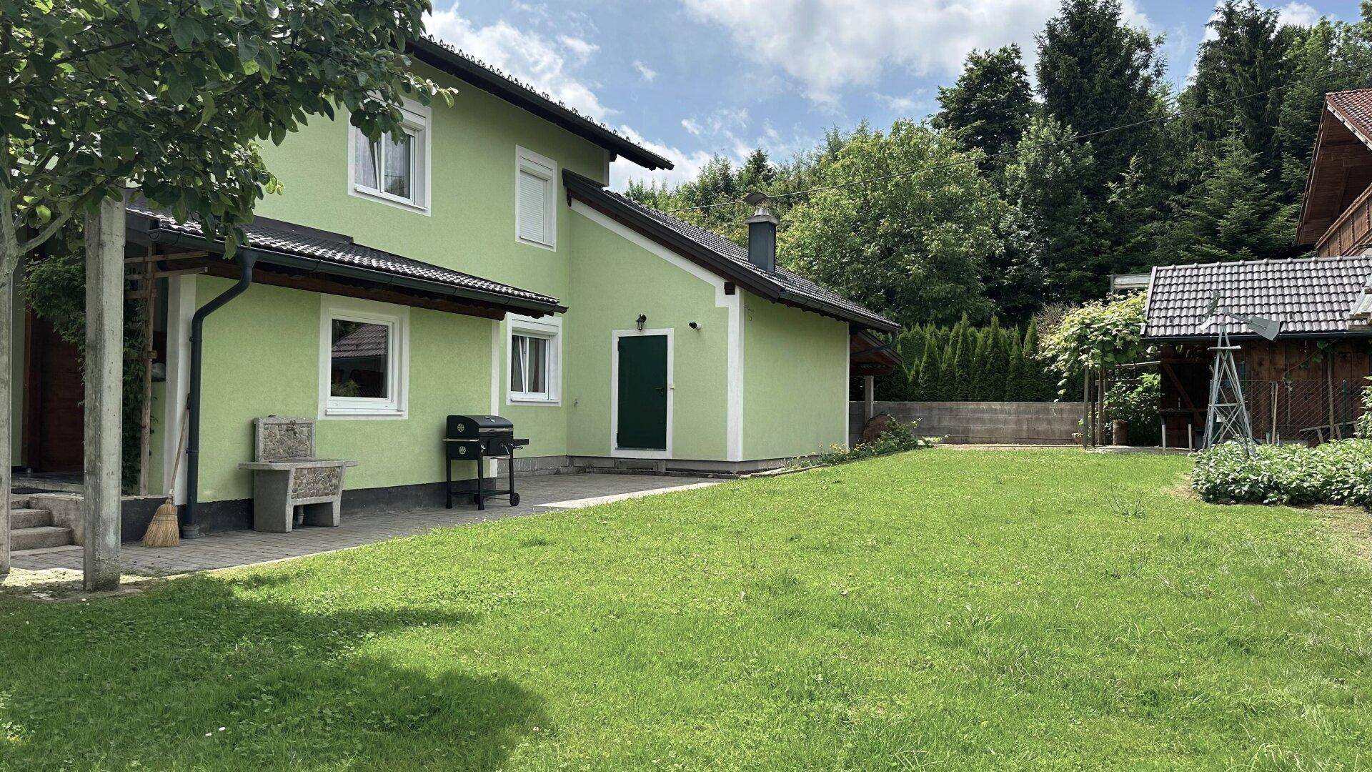 Großzügiger Gartenbereich mit Rasenfläche und einer kleinen Terrasse am hellgrünen Haus.